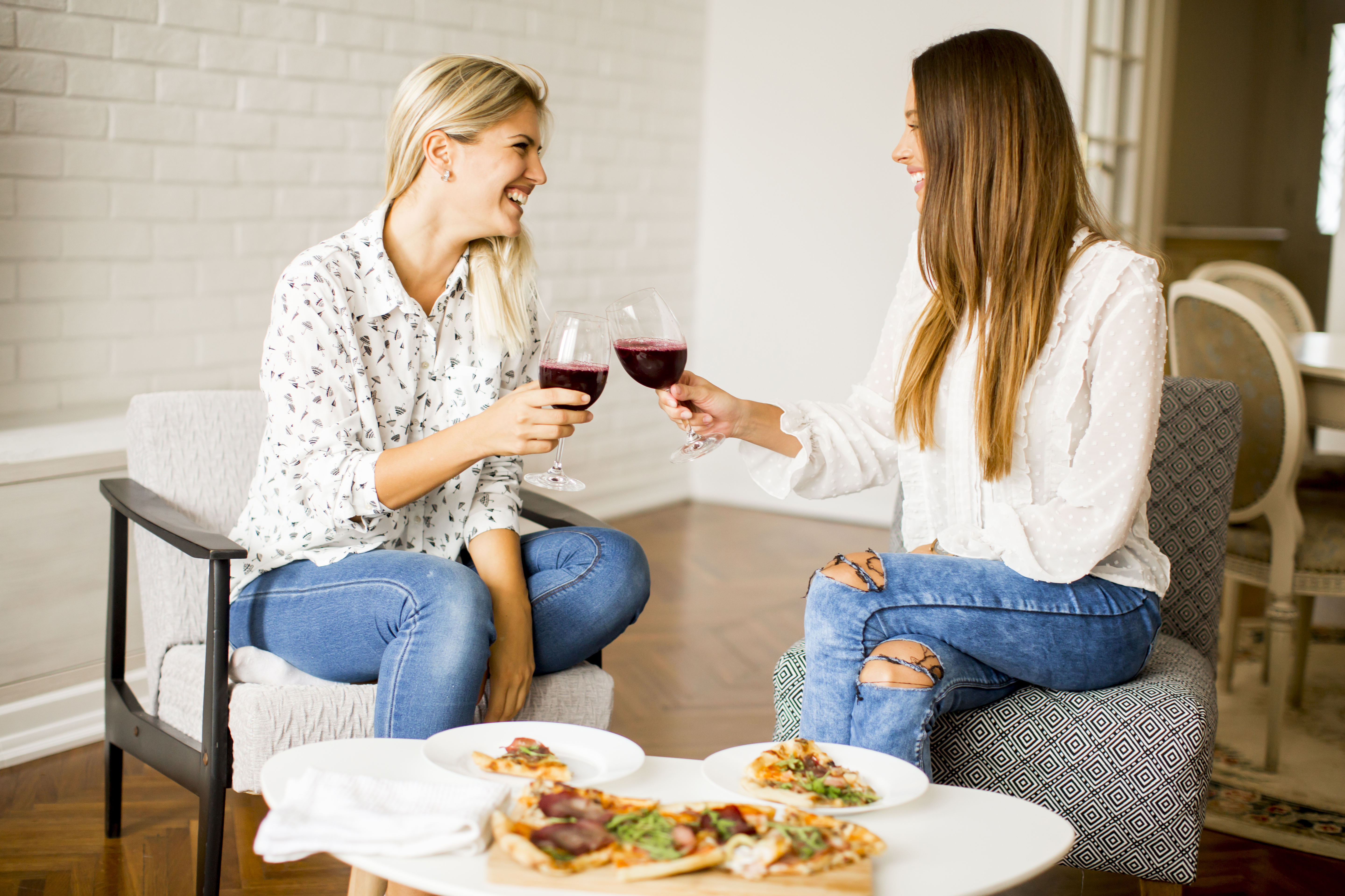 Hübsche junge Frauen essen Pizza und trinken Rotwein | Quelle: Getty Images