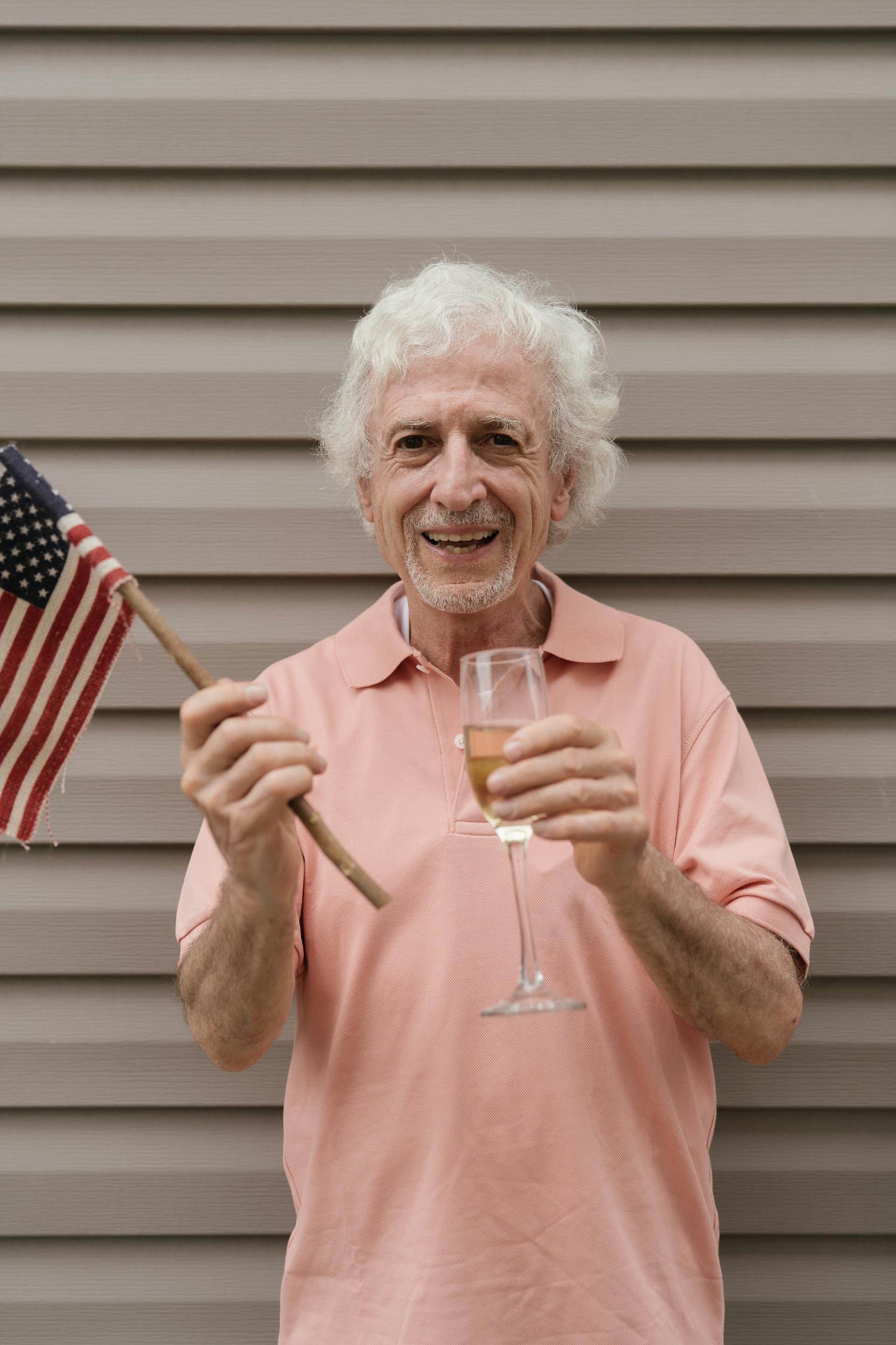 Ein älterer Mann hält die amerikanische Flagge und ein Glas Champagner in der Hand | Quelle: Pexels