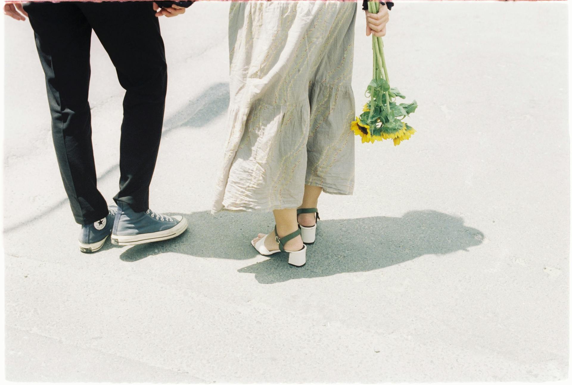 Eine Frau hält einen Strauß Sonnenblumen und geht mit ihrem Partner spazieren | Quelle: Pexels