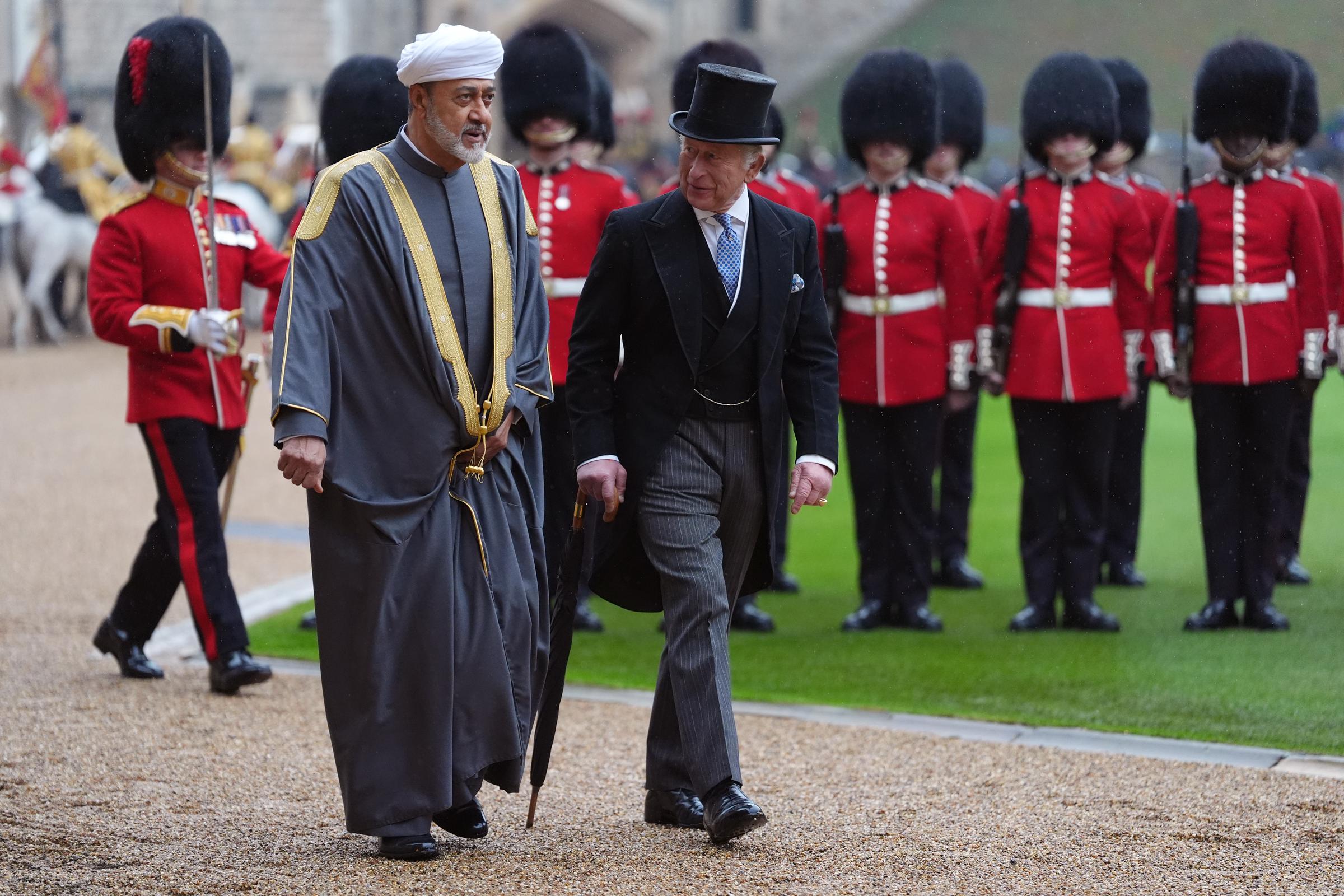 König Charles III. und Sultan Haitham bin Tarik von Oman inspizieren die Militärwache während der feierlichen Begrüßungszeremonie im Windsor Castle in Windsor, England, am 20. Oktober 2026. Während Gardisten in scharlachroten Uniformen und hohen Bärenfellmützen hinter ihnen in Formation stehen, sieht König Charles III. in einem schwarzen Morgenmantel, einer Nadelstreifenhose und einem Seidenzylinder klassisch elegant aus, während er einen Regenschirm hält und neben dem Sultan hergeht, der einen traditionellen grauen Bisht mit Goldstickerei und einen weißen Turban trägt. | Quelle: Getty Images
