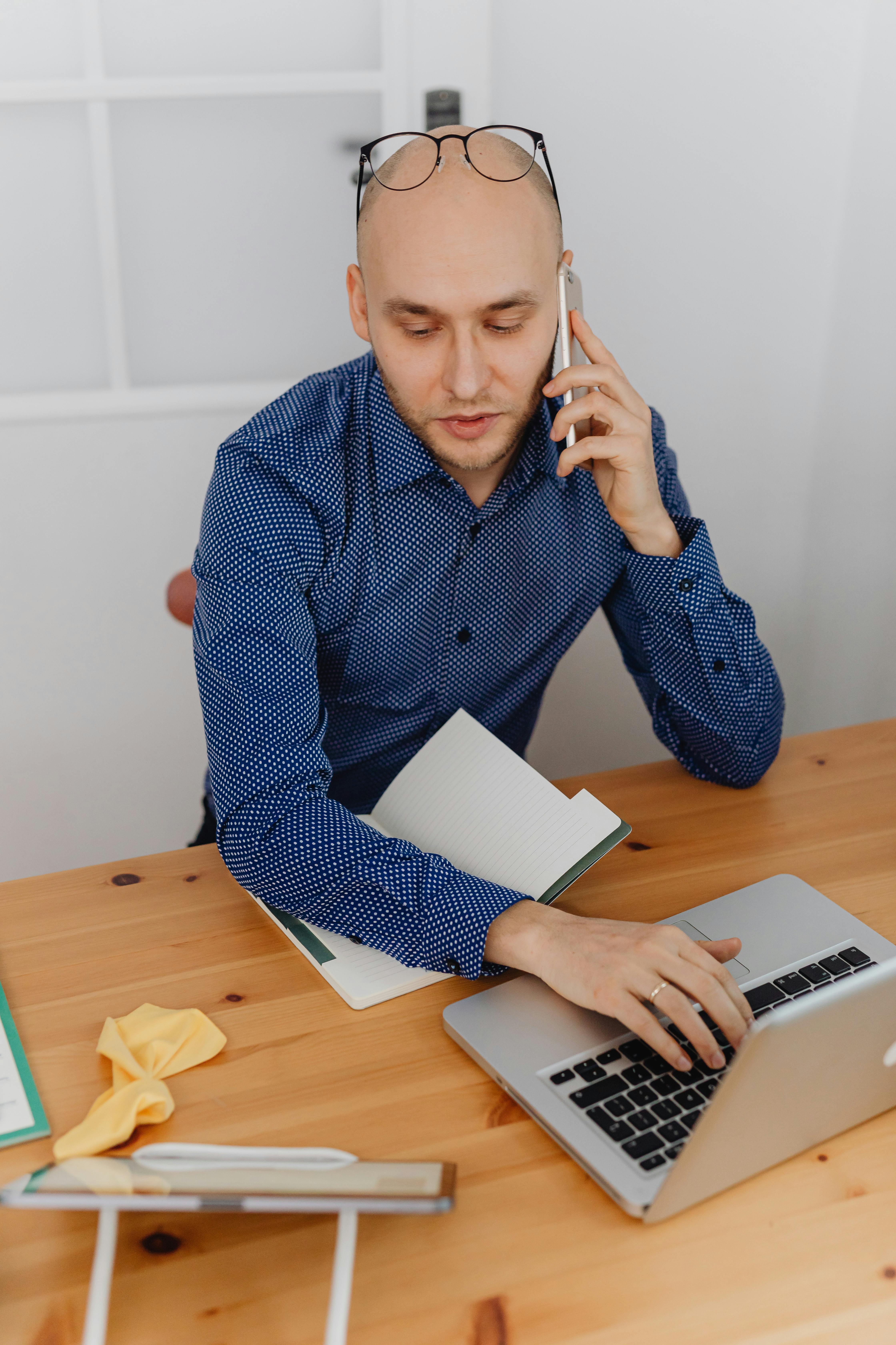Ein formell gekleideter Mann führt ein Telefonat, während er an einem Laptop arbeitet | Quelle: Pexels
