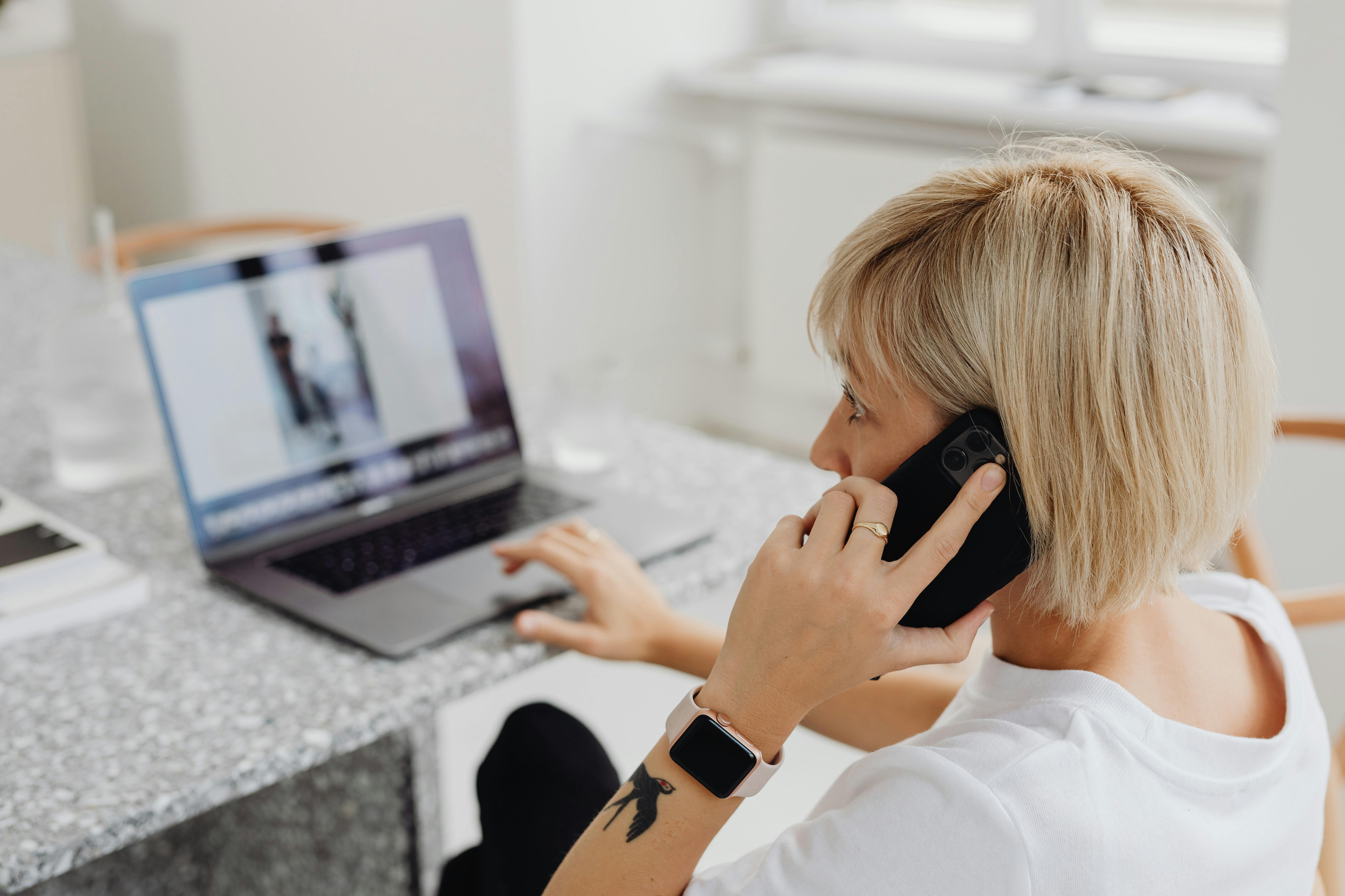 Eine Frau, die einen Laptop benutzt, während sie ein Telefonat führt | Quelle: Pexels