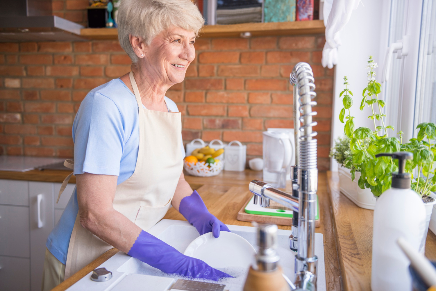 Eine lächelnde Seniorin beim Abwasch in der Küche | Quelle: Freepik