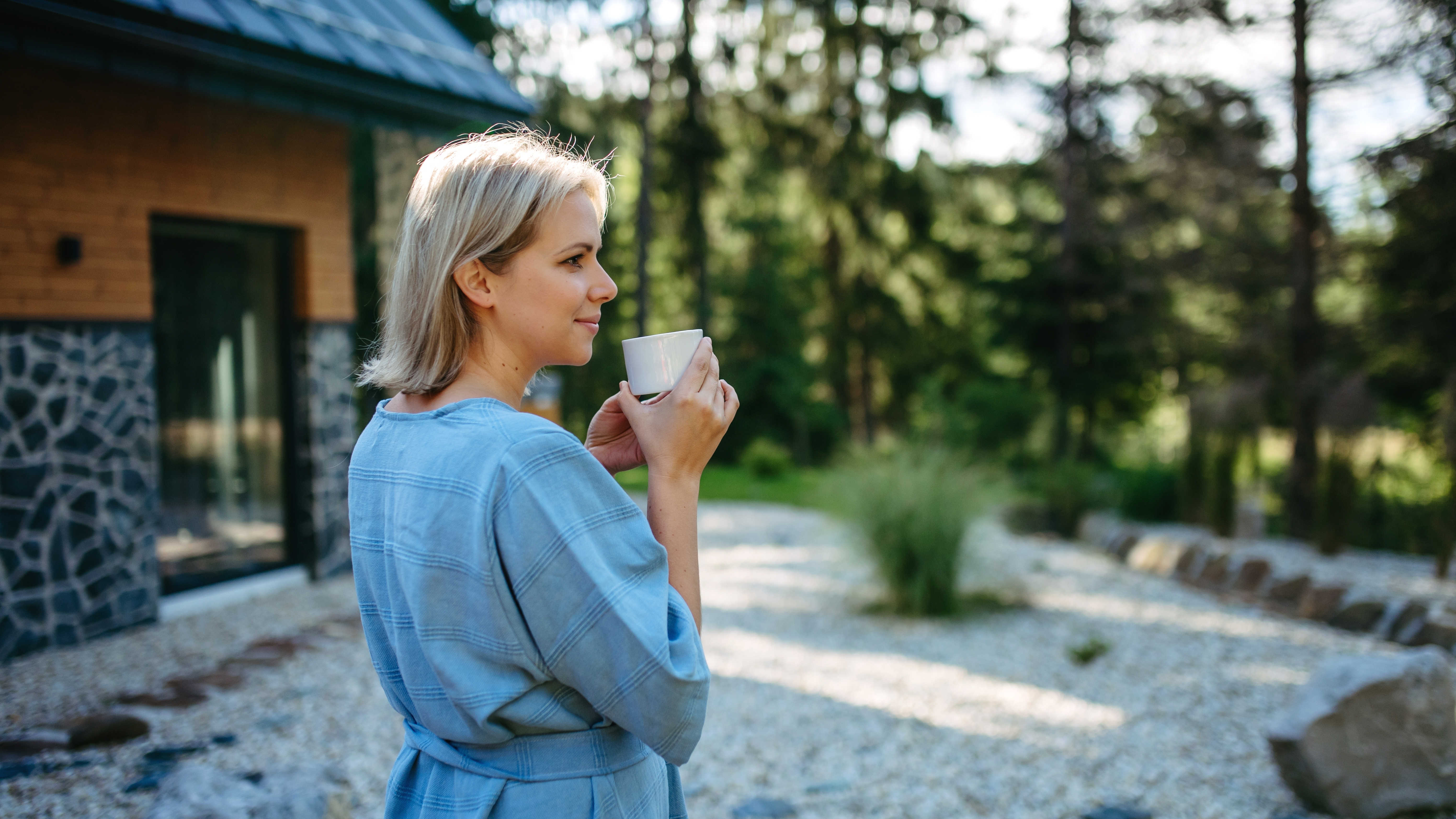 Eine Frau genießt eine Tasse Kaffee in einem Garten vor ihrem Haus | Quelle: Shutterstock