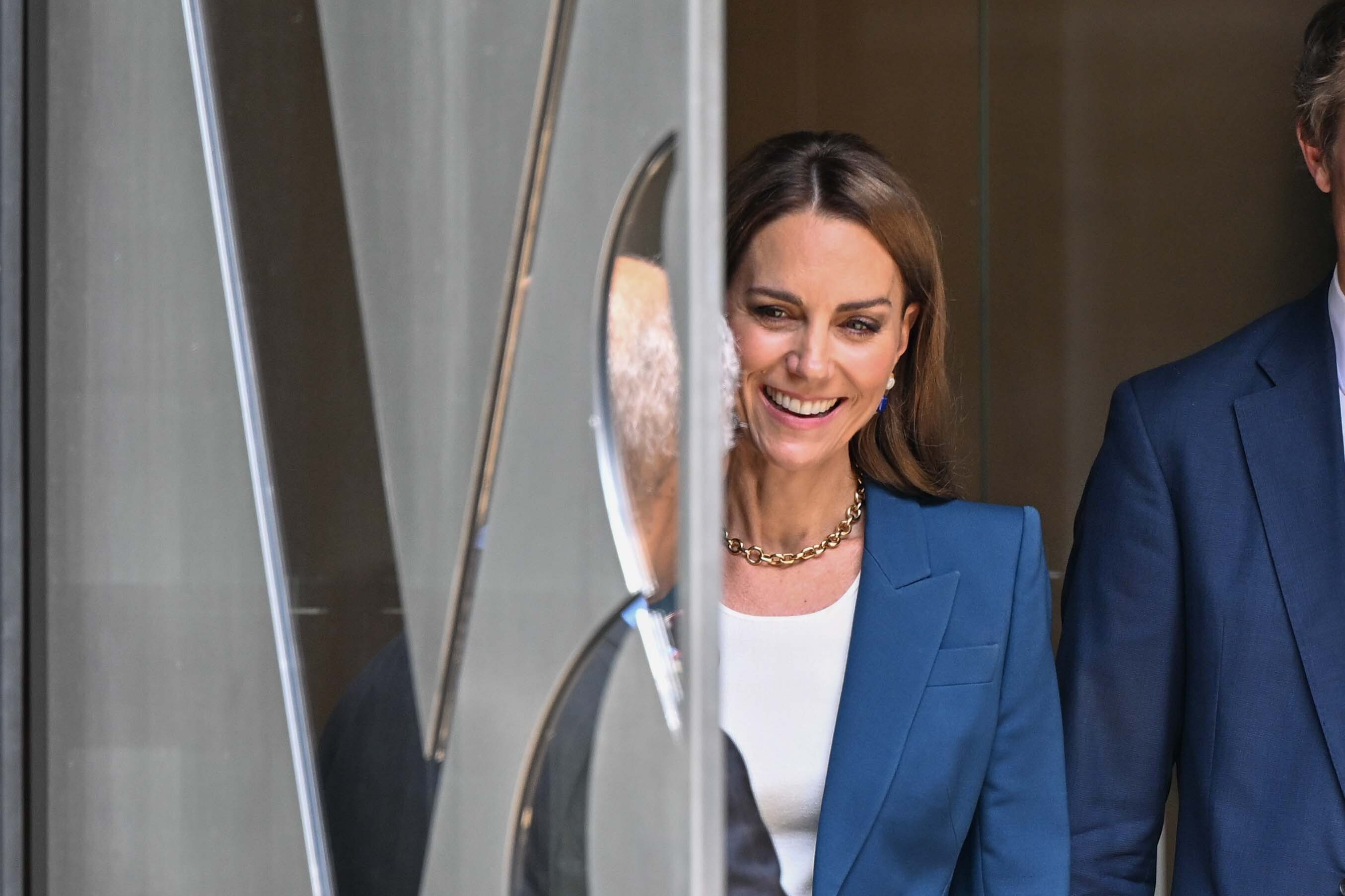 Prinzessin Catherine zeigt sich mit einem strahlenden Lächeln am Eingang des V&A East Storehouse. Sie trägt einen maßgeschneiderten blauen Anzug und ein weißes Oberteil. Gold- und Saphirschmuck verleihen ihrem modernen, zurückhaltenden Look eine raffinierte Note.