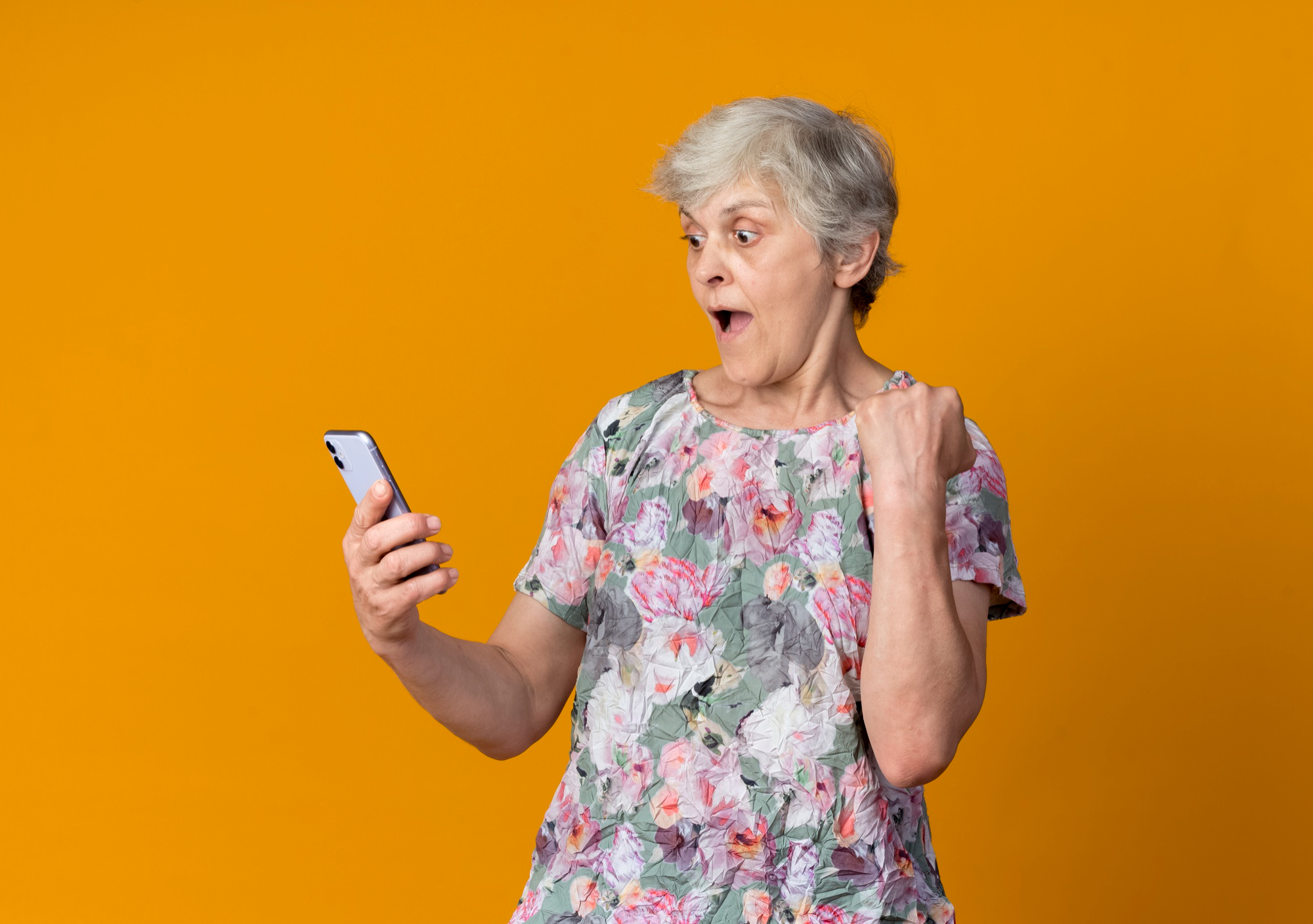 Eine ältere Frau reagiert geschockt, während sie auf ihr Telefon schaut | Quelle: Freepik