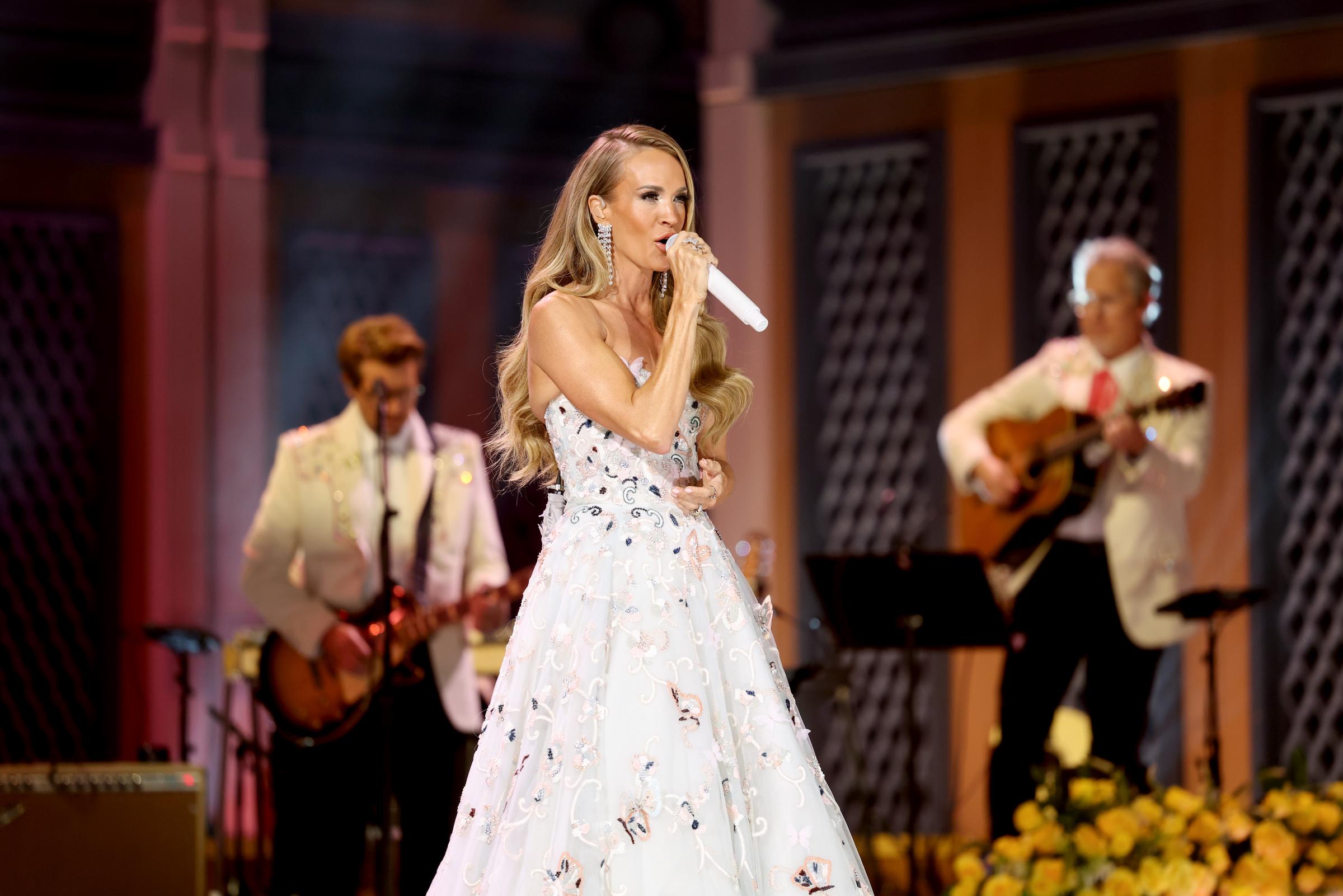 Carrie Underwood tritt während der Dolly-Parton-Hommage gemeinsam mit Musikern in weißen Jacken auf und trägt dabei ein mit Schmetterlingen besticktes Abendkleid als Teil der Hommage an die Country-Legende an diesem Abend. | Quelle: Getty Images.