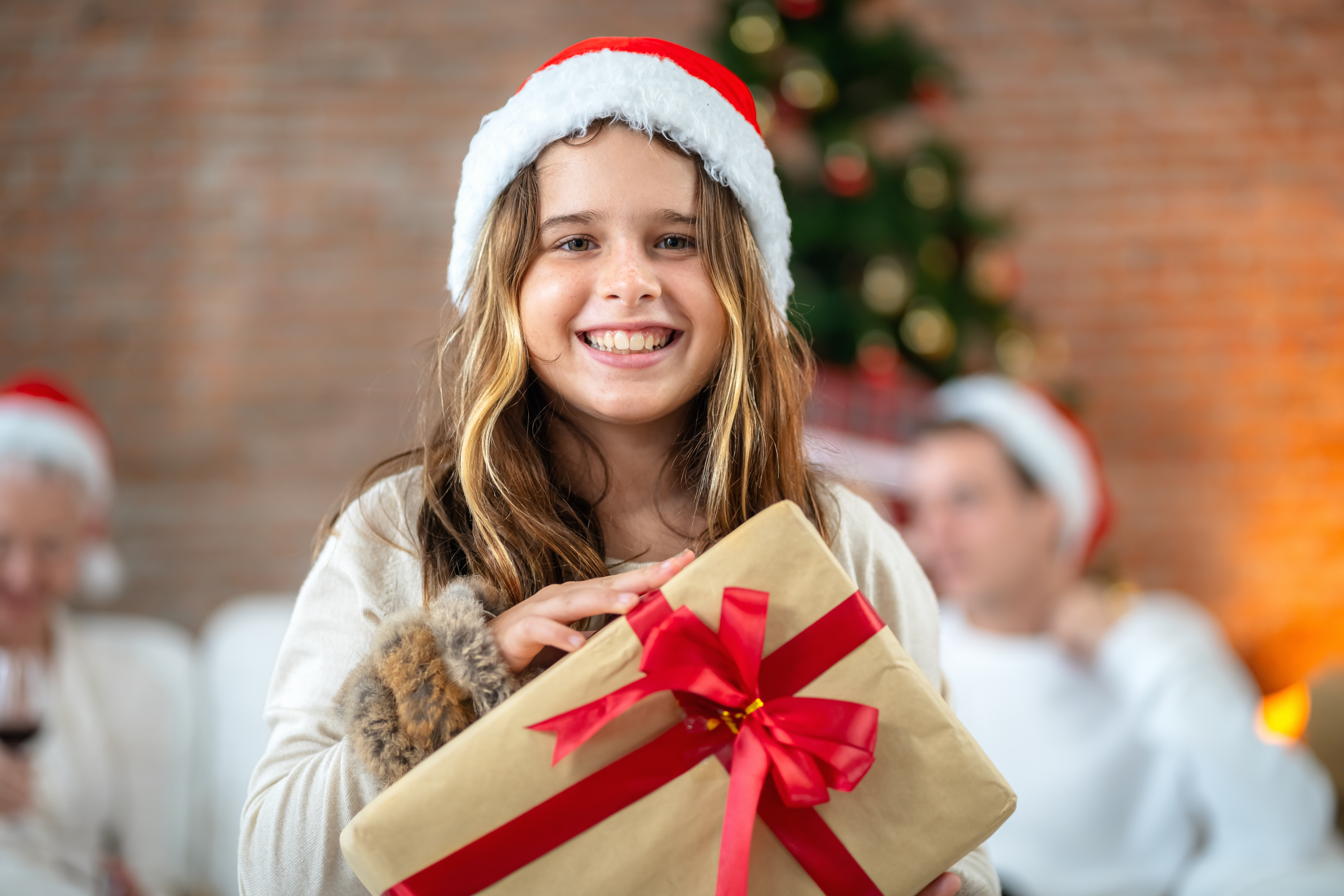 Ein junges Mädchen, das eine Geschenkbox in der Hand hält, lächelt am ersten Weihnachtstag glücklich. | Quelle: Getty Images