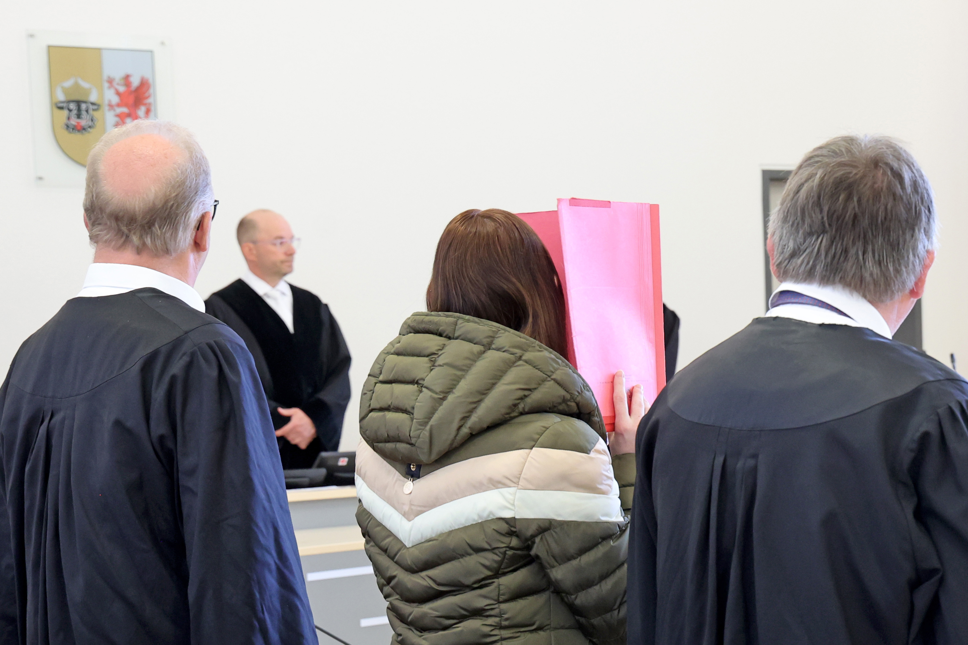 Die Angeklagte verbirgt ihr Gesicht beim Prozessauftakt am 28. April 2026 in Rostock ihr Gesicht hinter einem roten Ordner. | Quelle: Getty Images