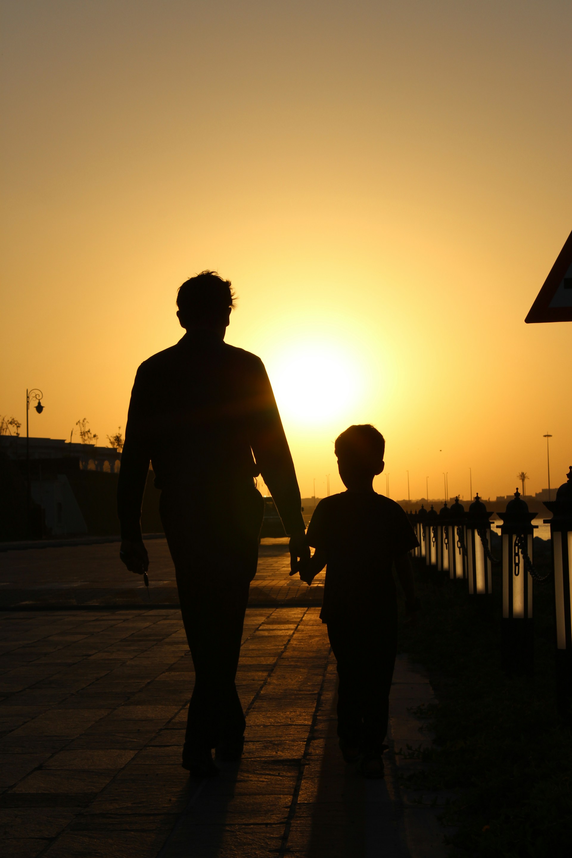 Silhouette eines Vaters und seines Sohnes, die auf der Straße gehen | Quelle: Unsplash