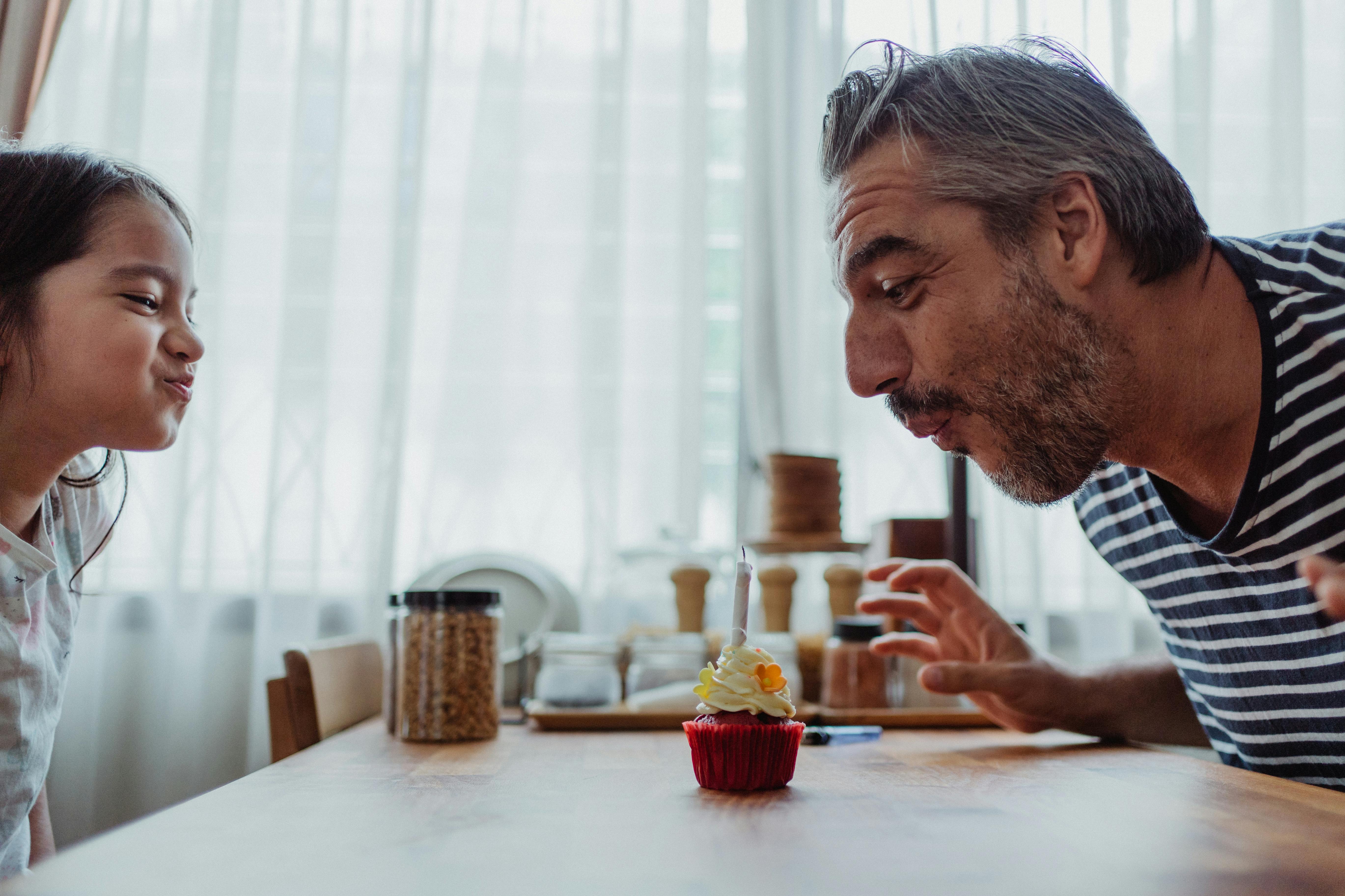 Ein Mann und ein kleines Mädchen blasen eine Kerze auf einem Cupcake an | Quelle: Pexels