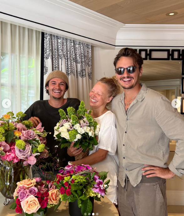 Pamela Anderson strahlt vor Freude neben ihren Söhnen Brandon Thomas Lee und Dylan Jagger Lee, umgeben von üppigen Blumenarrangements. Mit einem Strauß weißer Rosen und Grünpflanzen in der Hand lacht sie liebevoll mit den Jungs, die ihr dabei geholfen haben, sich ein friedliches Leben und einen Garten auf Vancouver Island aufzubauen. Um den Familienzusammenhalt zu feiern, für dessen Erhalt sie sich stets eingesetzt hat, schrieb sie zu ihrem Muttertags-Post: „Frieden, Liebe, Freude … Ein Segen für alle Mütter auf der Welt 🤍“. | Quelle: Instagram/pamelaanderson