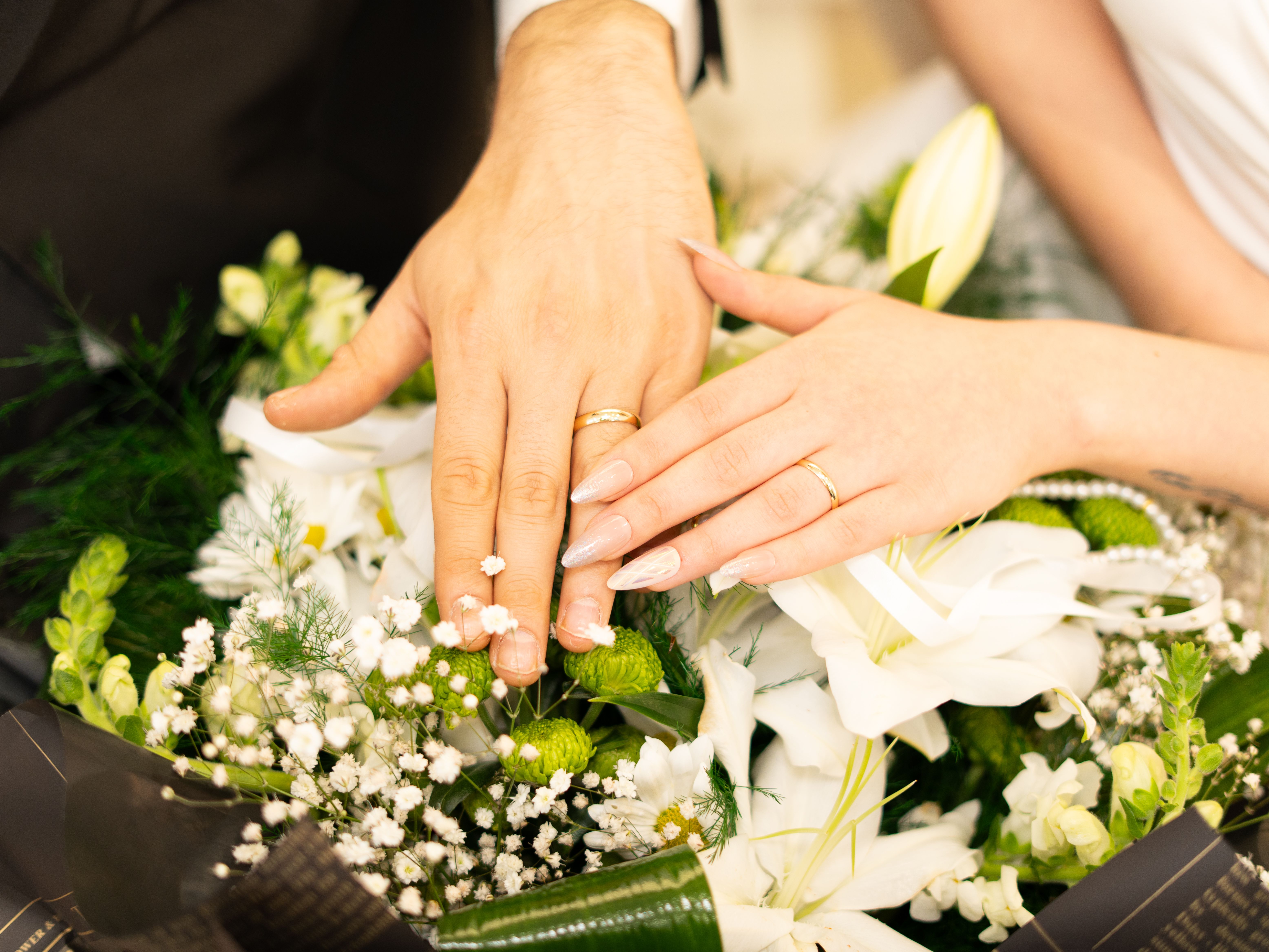 Nahaufnahme von Händen mit Eheringen, die auf einem Blumenstrauß ruhen | Quelle: Pexels