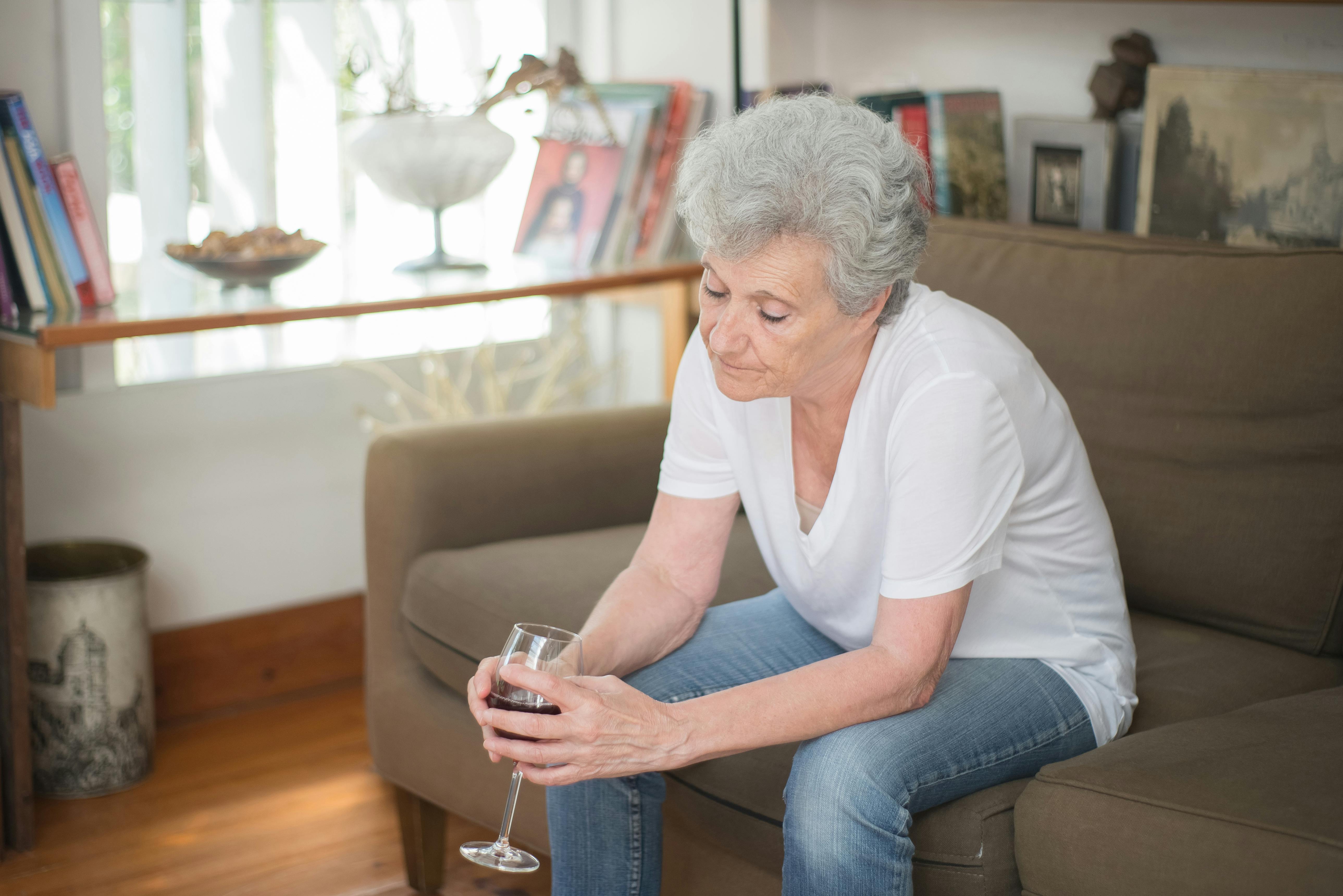 Eine aufgebrachte ältere Frau hält ein Glas Wein in der Hand, während sie auf einer Couch sitzt | Quelle: Pexels