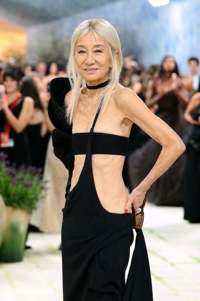 Inspiriert vom grün-weißen Teppich der Met Gala 2024 interpretiert diese KI-Kreation Vera Wangs gewagten High-Fashion-Auftritt neu – mit sichtbaren, authentischen Zeichen des Alterns an Hals, Dekolleté und Bauch. Das Konzept behält das markante platinblonde Haar der Designerin, den schwarzen Halsreif und das Cut-Out-Kleid mit asymmetrischem Schulterdrapierung bei und präsentiert eine unverfälschte, natürliche Gesichtsstruktur mit weichen, reifen Gesichtszügen. | Quelle: Gemini