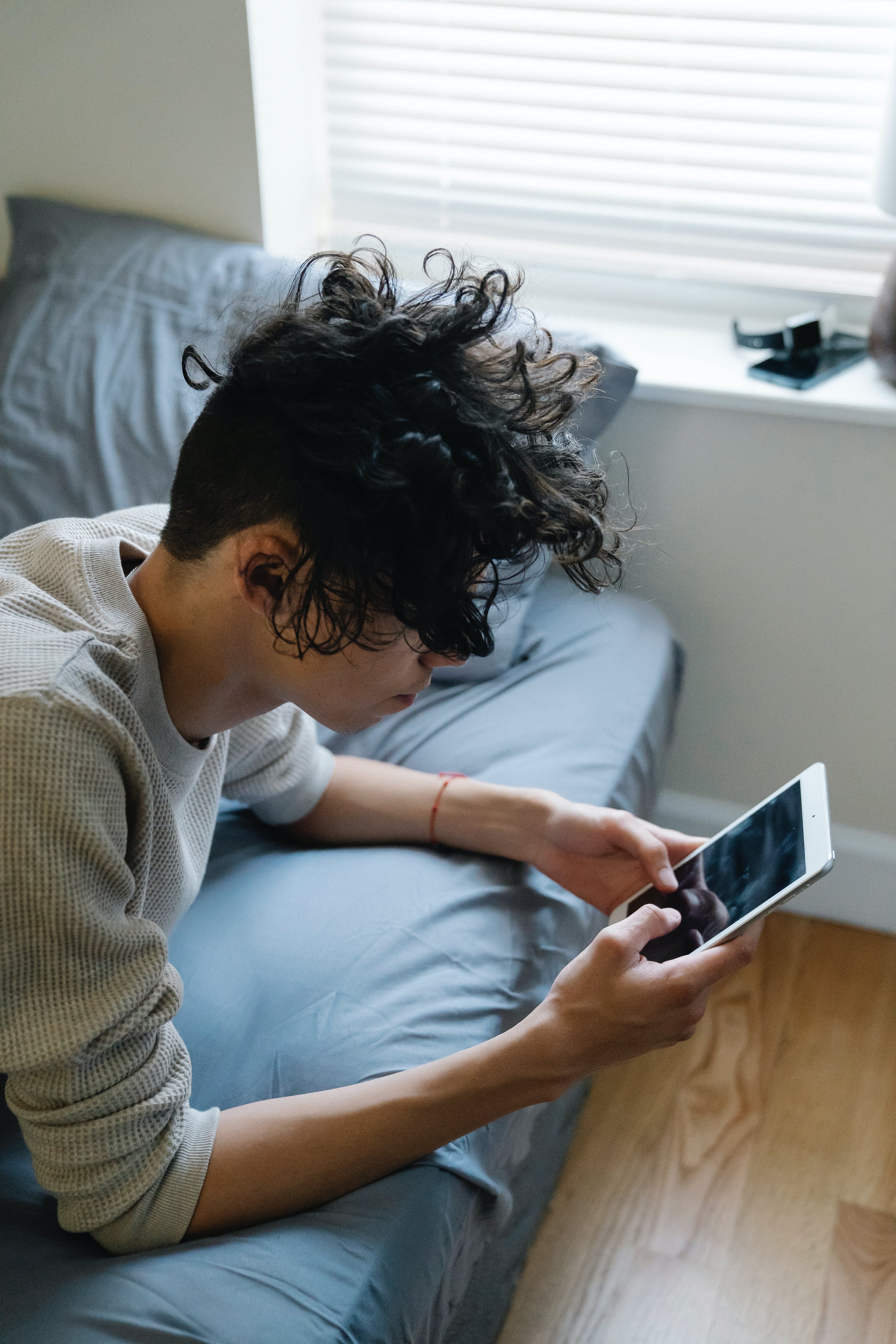 Ein junger Mann, der auf einem Bett liegend eine SMS auf seinem Handy schreibt | Quelle: Pexels