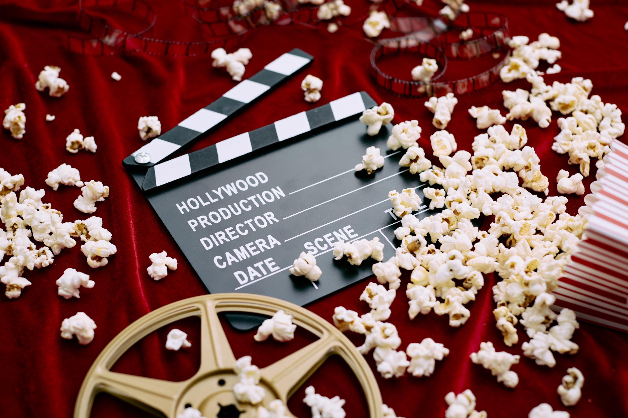 Eine Klappe, eine Filmrolle, ein Film und verschüttetes Popcorn auf einem roten Satin-Hintergrund | Quelle: Getty Images