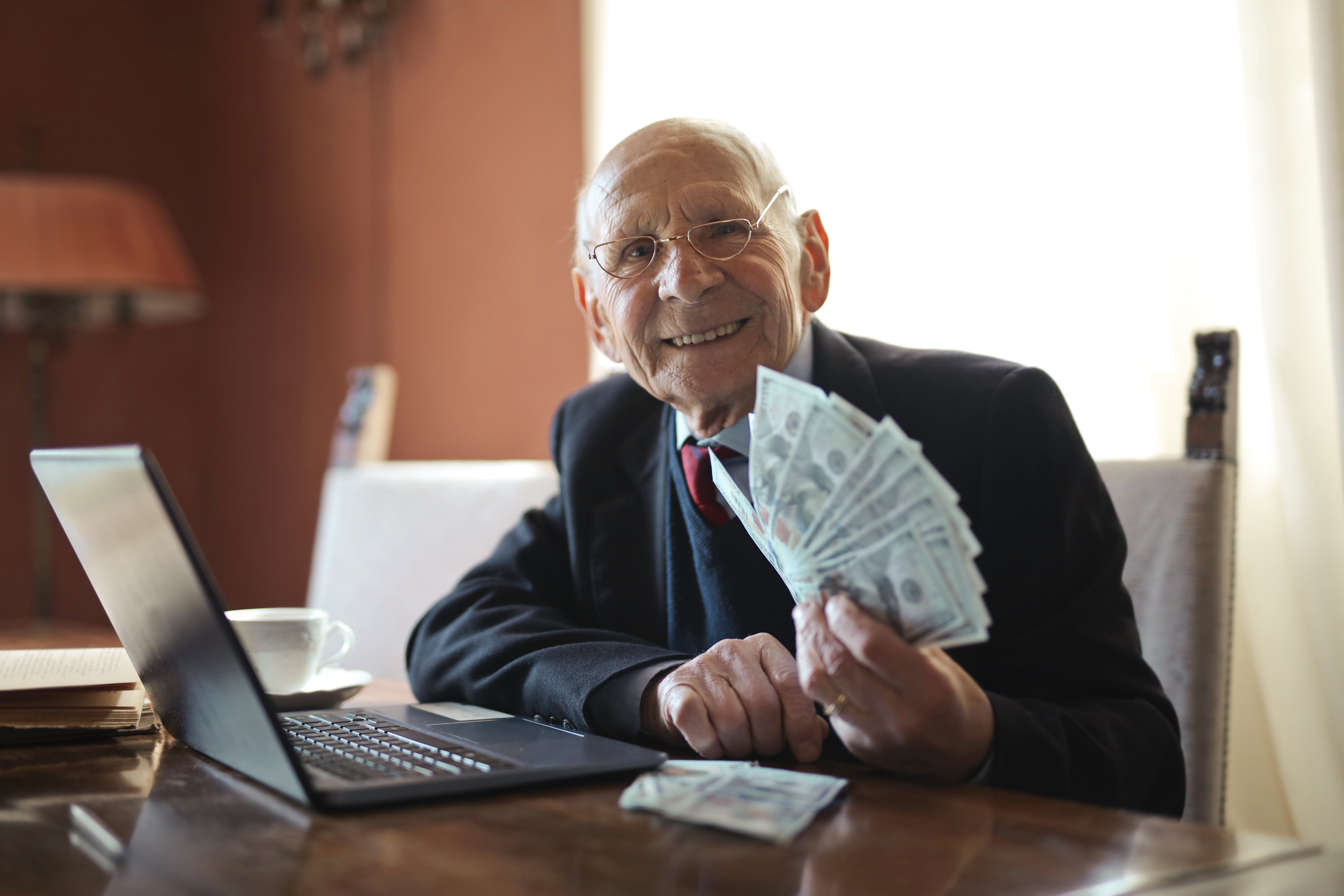 Ein älterer Mann lächelt und hält Geld in der Hand. | Quelle: Pexels