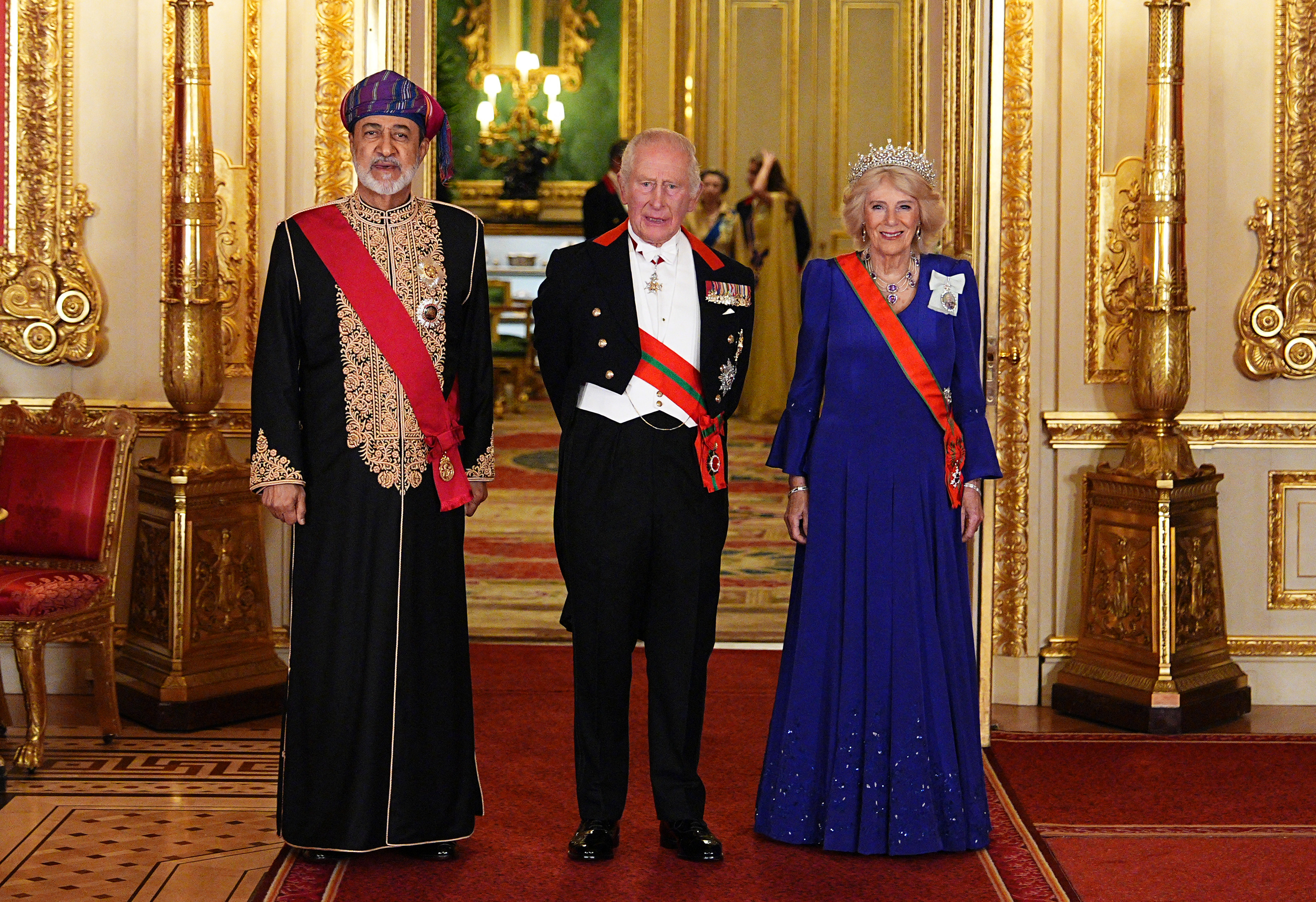 Sultan Haitham bin Tarik von Oman posiert zusammen mit König Charles III. und Königin Camilla im Windsor Castle vor dem prunkvollen Staatsbankett am 20. Oktober 2026 in Windsor, England. Umgeben von kunstvoller, vergoldeter Saalausstattung trägt König Charles III. einen formellen Abendfrack mit Militärmedaillen und Ordensschärpen neben dem Sultan, der eine aufwendig goldbestickte schwarze Festrobe, eine rote zeremonielle Schärpe und einen farbenfrohen traditionellen Massar-Turban trägt, während Königin Camilla in einem blauen Plissee-Kleid glänzt, gekrönt von der funkelnden belgischen Saphir-Tiara und einer orangefarbenen Ordensschärpe. | Quelle: Getty Images