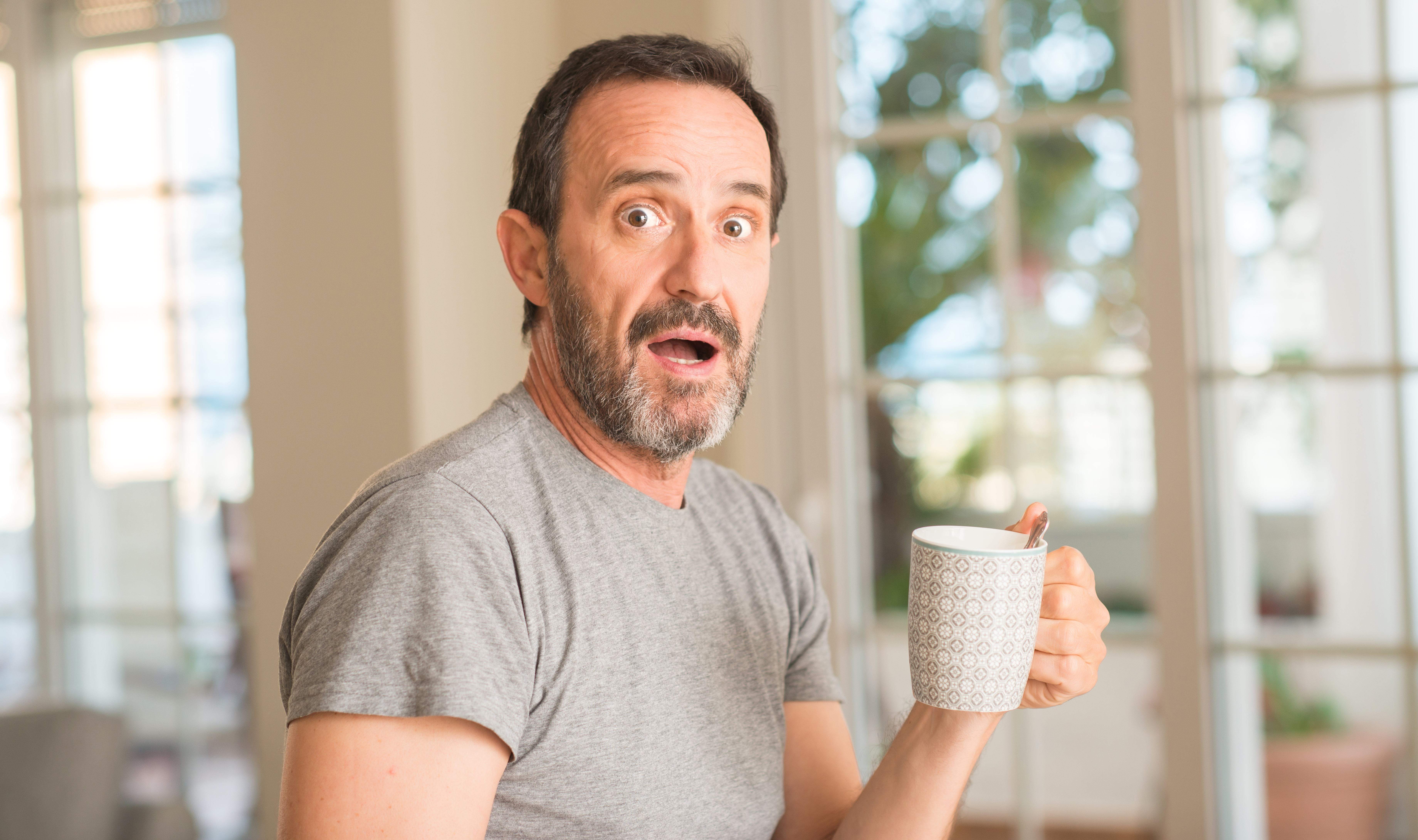 Mann mittleren Alters, der Kaffee in einer Tasse trinkt, erschrocken mit einem überraschten Gesicht, ängstlich und aufgeregt mit Angstausdruck | Quelle: Getty Images