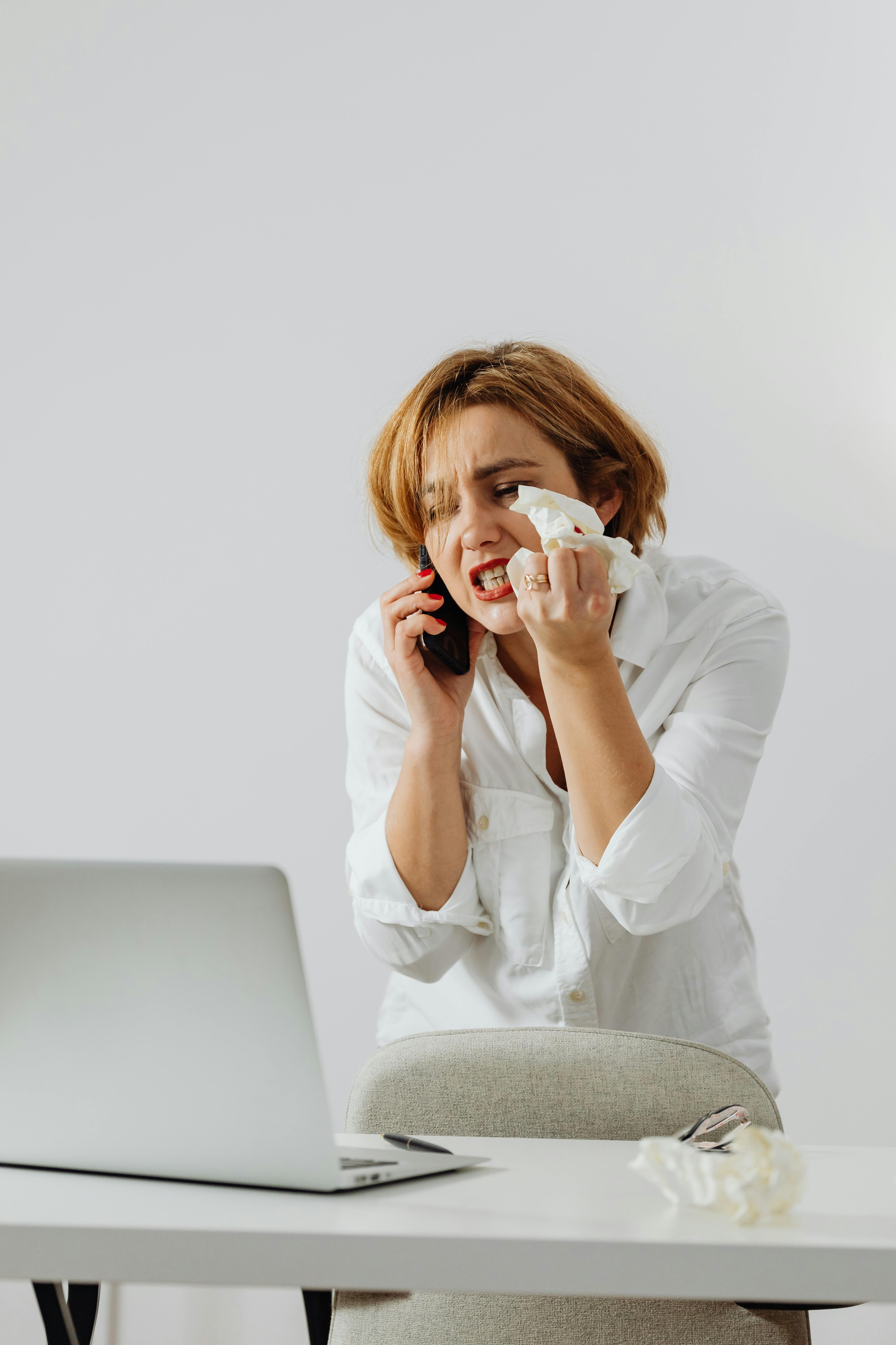 Frau weint vor ihrem Laptop in ihr Telefon | Quelle: Pexels