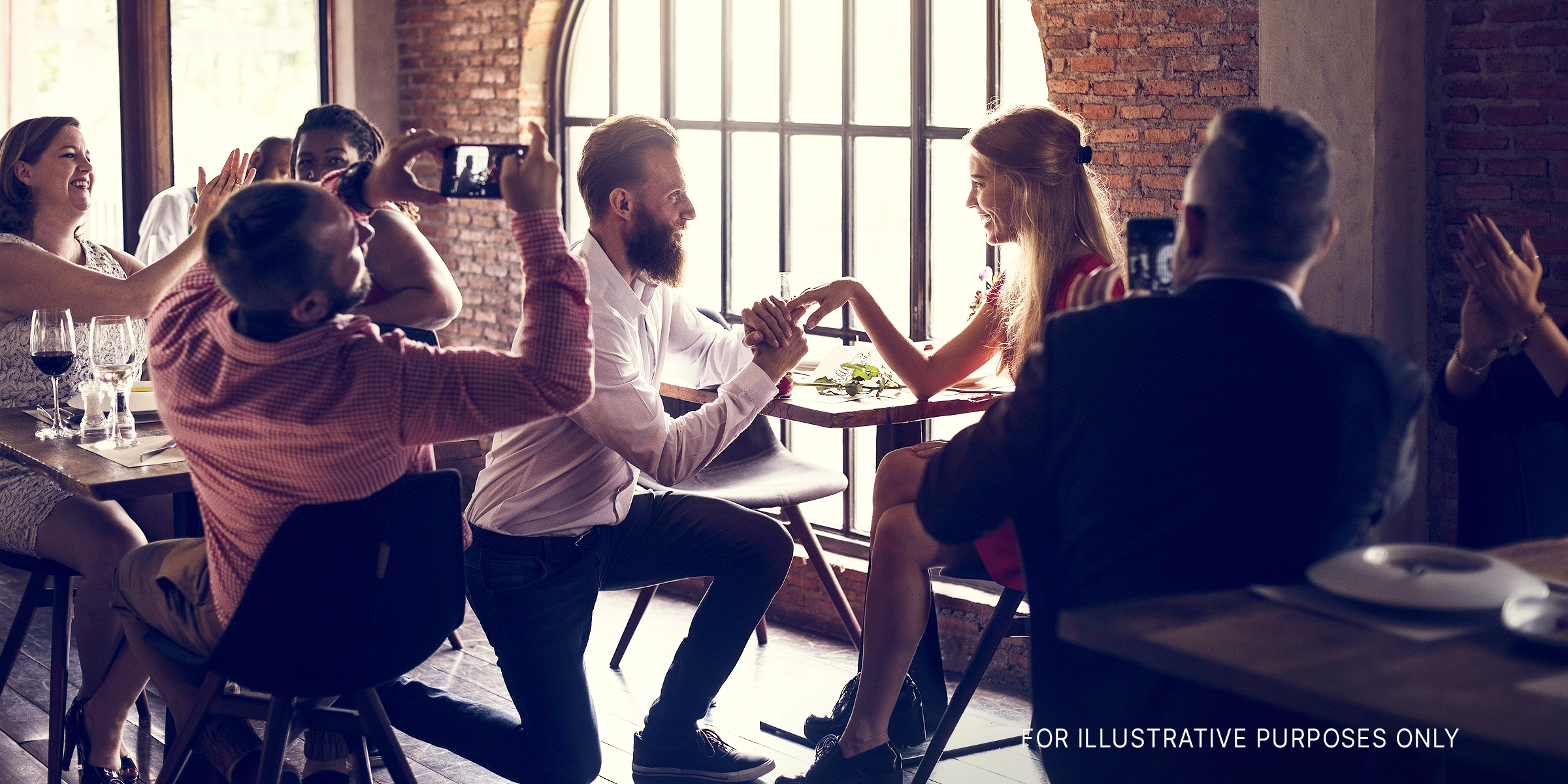 Ein Mann kniet in einem Restaurant und macht ihr einen Antrag. | Quelle: Shutterstock