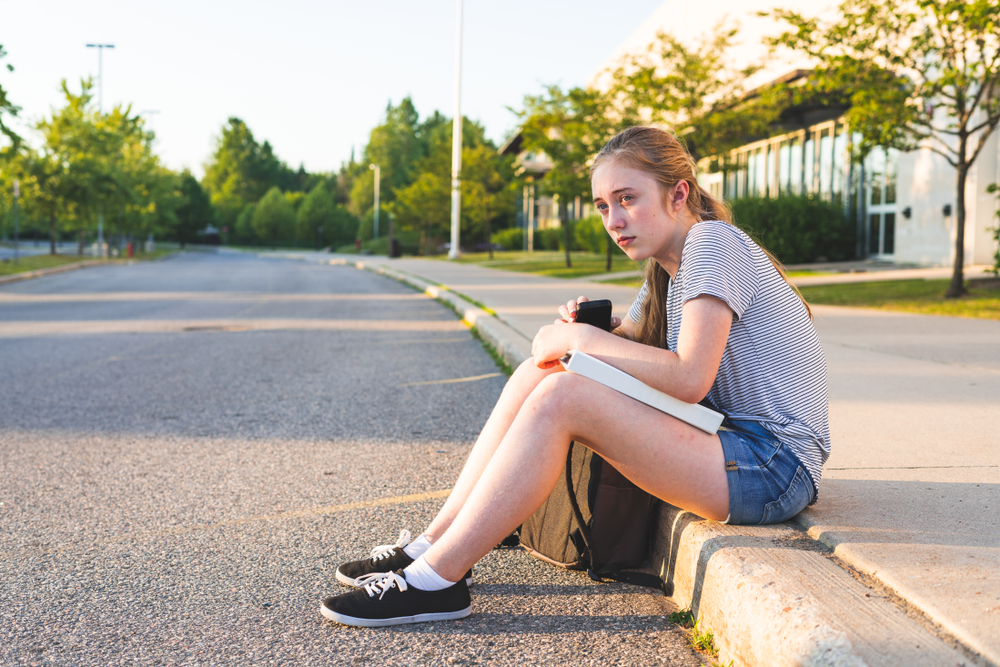 Ein junges Mädchen sitzt am Straßenrand | Quelle: Shutterstock