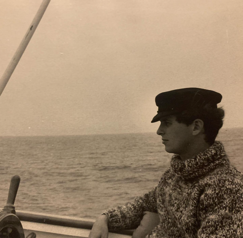 Ein altes Foto zeigt Stephen Wyle, den Vater von Noah Wyle, mit einer Matrosenmütze und einem dicken Strickpullover, wie er an Bord eines Bootes sitzt, während sich hinter ihm das Meer erstreckt. | Quelle: Instagram/therealnoahwyle