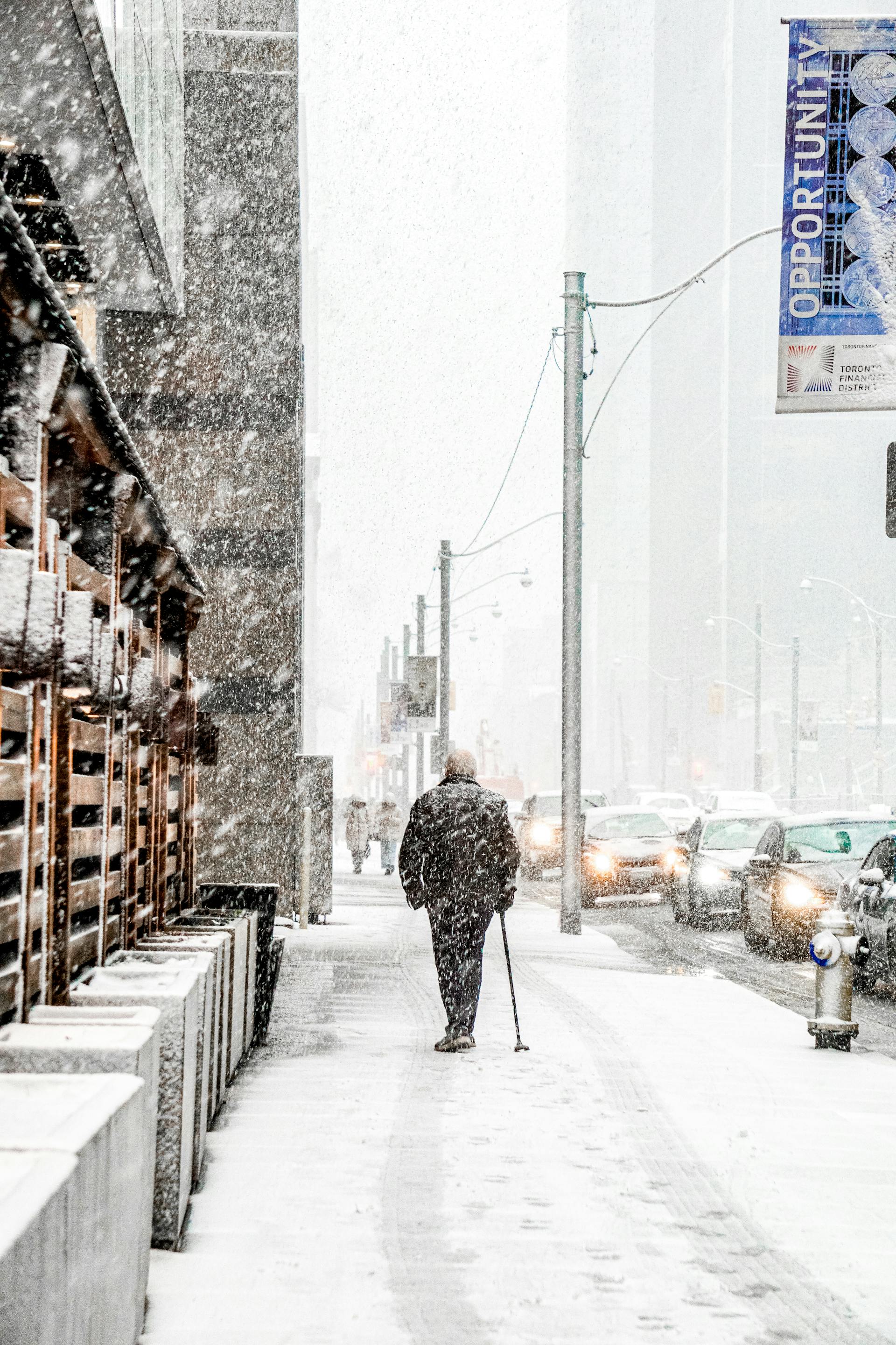 Rückansicht eines alten Mannes, der bei Schneefall auf dem Gehweg geht | Quelle: Pexels