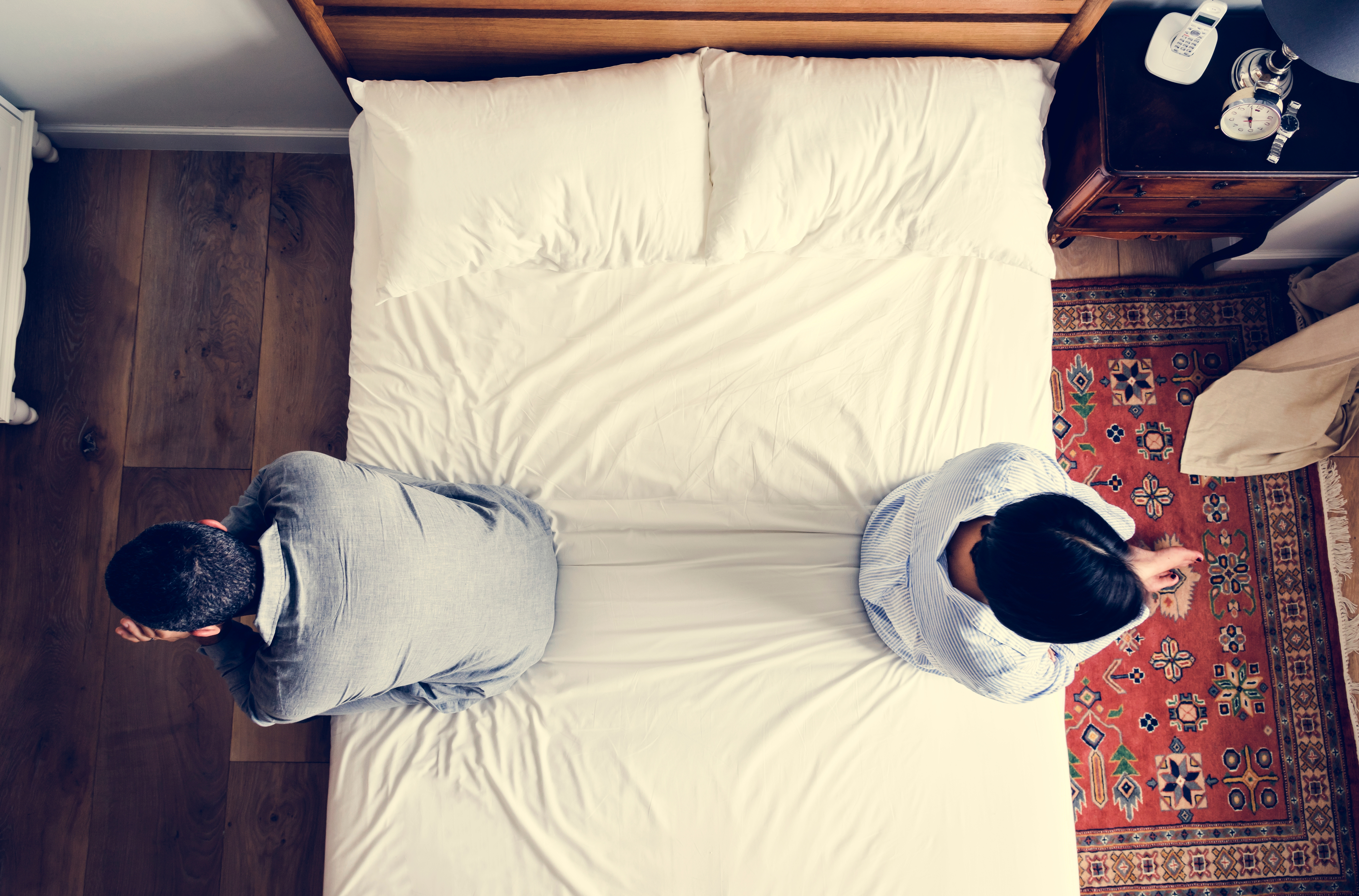 Ein Paar, das nach einem Streit auf den gegenüberliegenden Enden seines Bettes sitzt | Quelle: Shutterstock