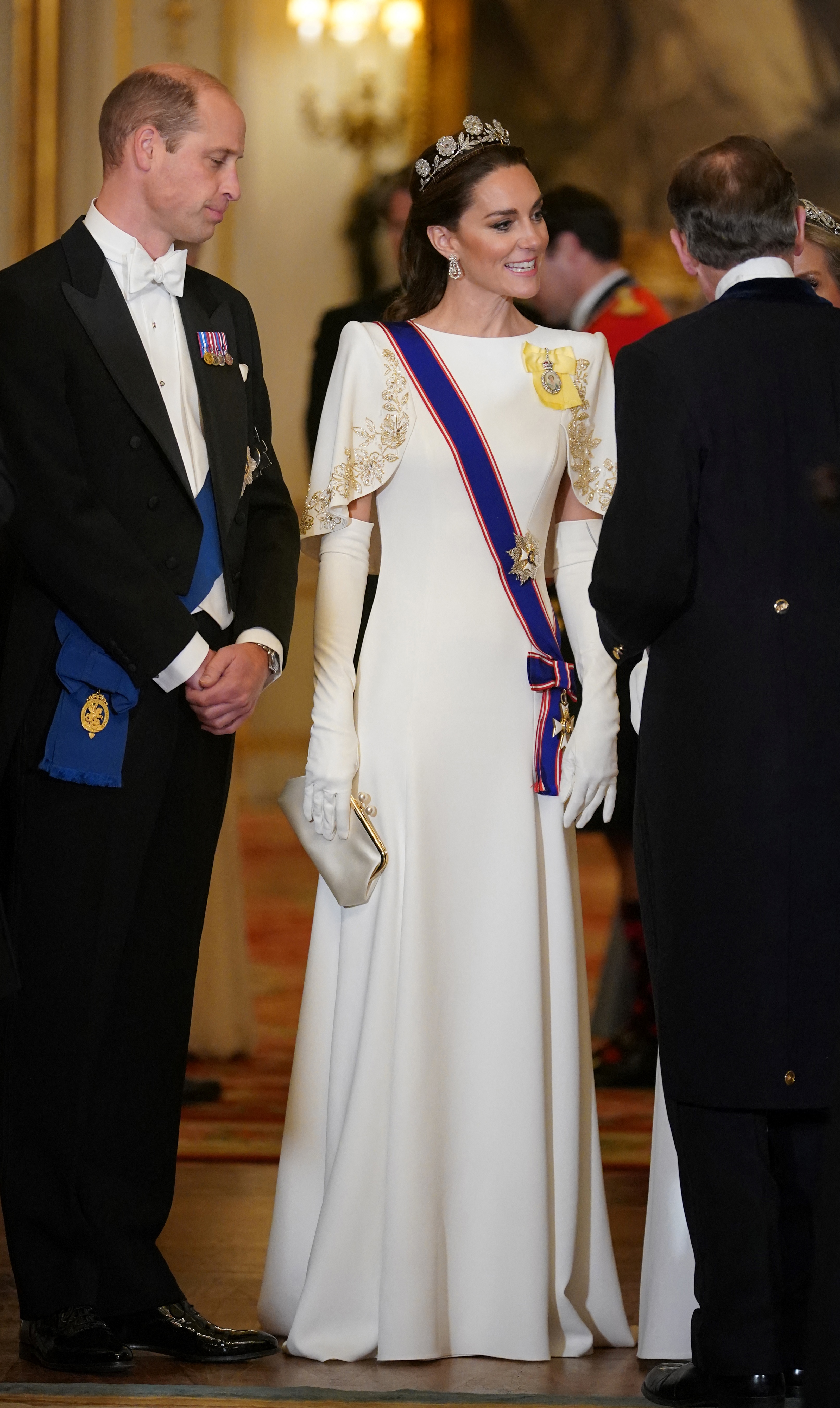 Prinz William und Catherine, Prinzessin von Wales, treffen am 21. November 2023 im Buckingham Palace zum Staatsbankett zu Ehren des südkoreanischen Präsidenten Yoon Suk Yeol und der First Lady Kim Keon Hee ein. Catherine strahlt in einem maßgeschneiderten weißen Jenny-Packham-Kleid mit goldbestickten Flügelärmeln, weißen Opernhandschuhen und der historischen Strathmore-Rose-Tiara, dazu trägt sie die Diamantohrringe und die königlichen Insignien von Königin Elizabeth II., während William neben ihr in einem klassischen schwarzen Frack und mit weißer Krawatte steht. | Quelle: Getty Images
