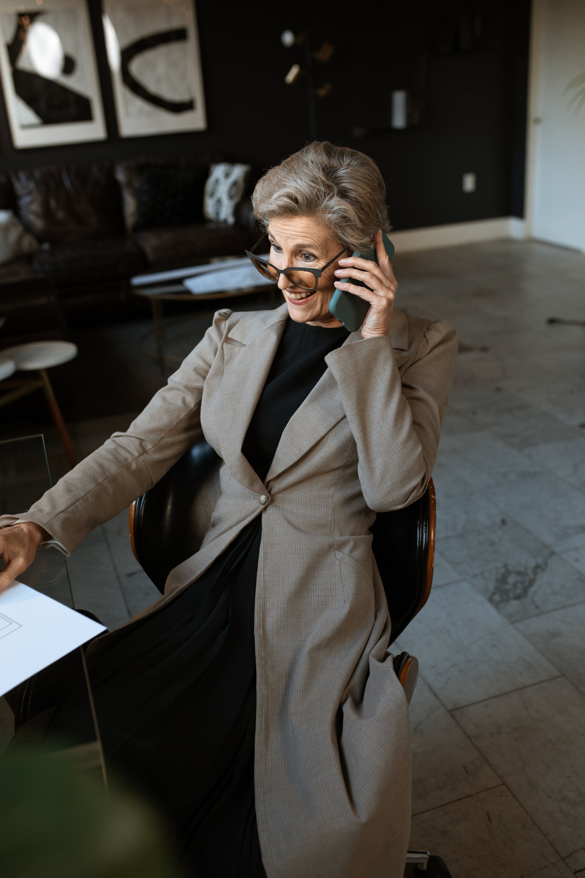 Eine ältere Frau in einem grauen Mantel sitzt beim Telefonieren auf einem Stuhl | Quelle: Pexels