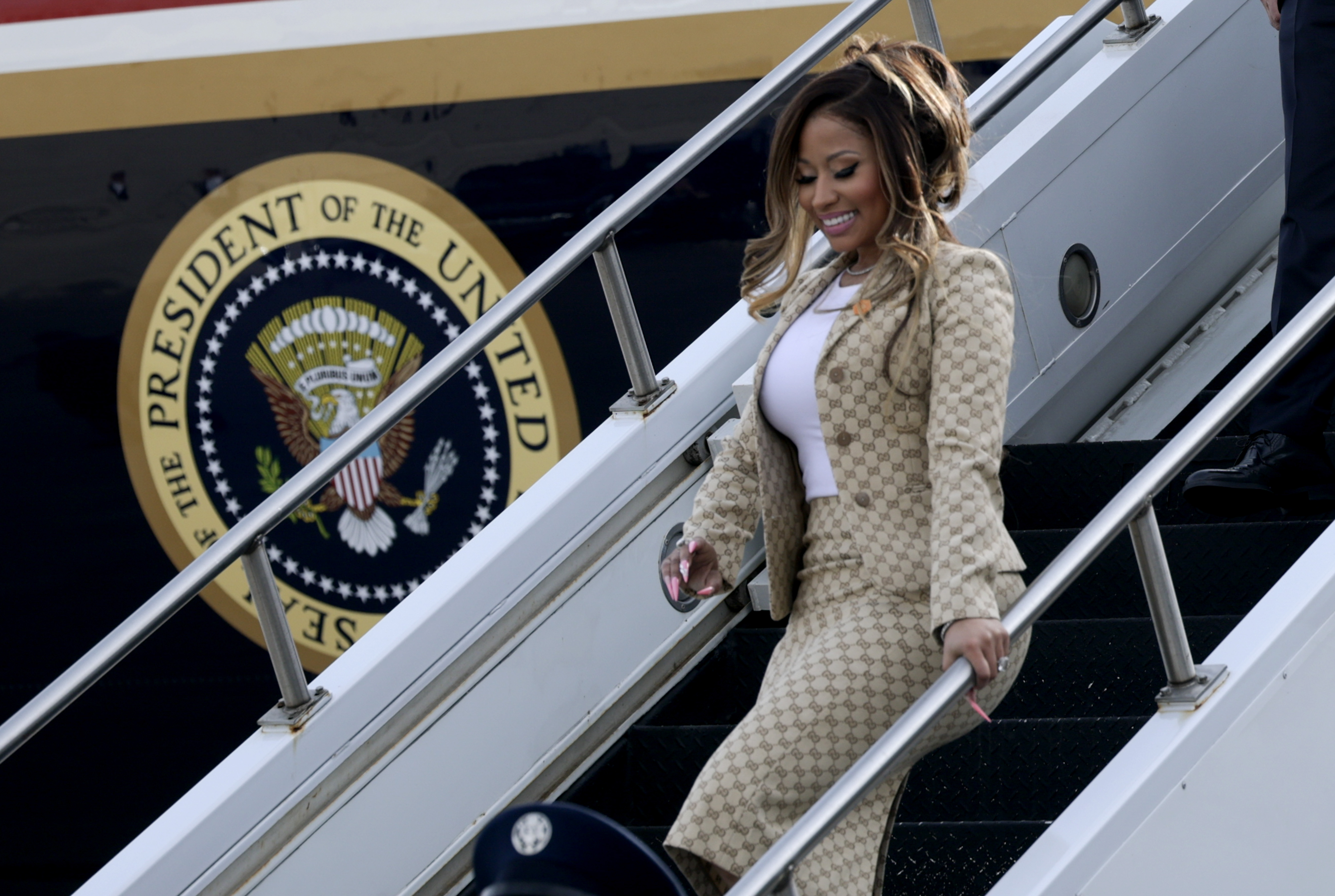 Nicki Minaj lächelt, als sie die Flugzeugtreppe hinunterkommt, während hinter ihr das offizielle Präsidentenwappen deutlich zu sehen ist – eine ungewöhnliche Ankunft für eine Rapperin, deren öffentliche Auftritte man eher mit Konzertbühnen und roten Teppichen in Verbindung bringt. | Quelle: Getty Images