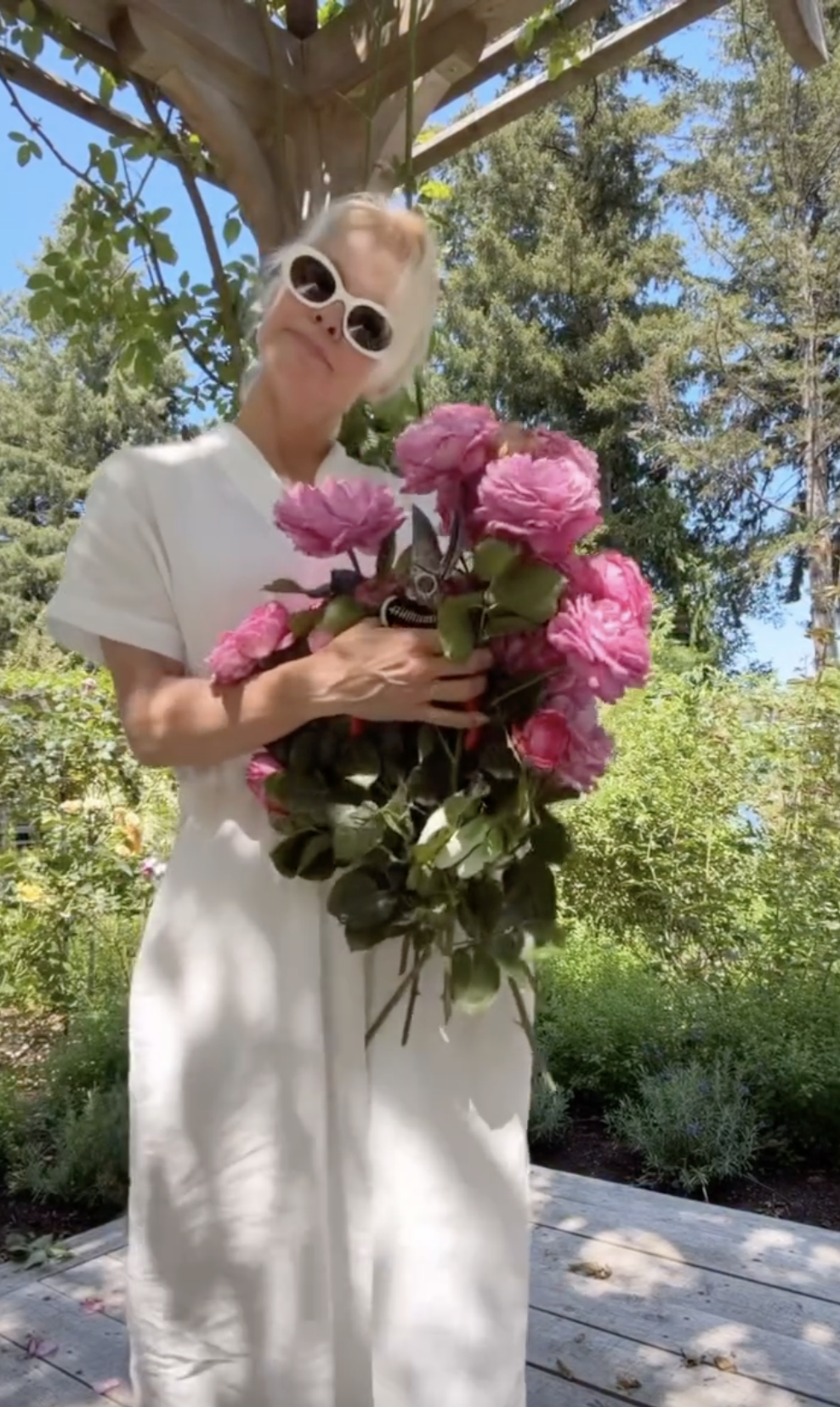 Pamela Anderson posiert verspielt unter einer Gartenlaube in Arcady und hält eine Gartenschere sowie ein riesiges Bündel frisch gepflückter rosa Rosen vor ihrem weißen Leinenkleid. Mit einer auffälligen weißen, ovalen Sonnenbrille verkörpert sie mühelos die Freude am Gärtnern und präsentiert stolz die Blüten, die sie aus ihrem blühenden, 15.000 Quadratfuß großen Rückzugsort geerntet hat. | Quelle: Instagram/pamelaanderson