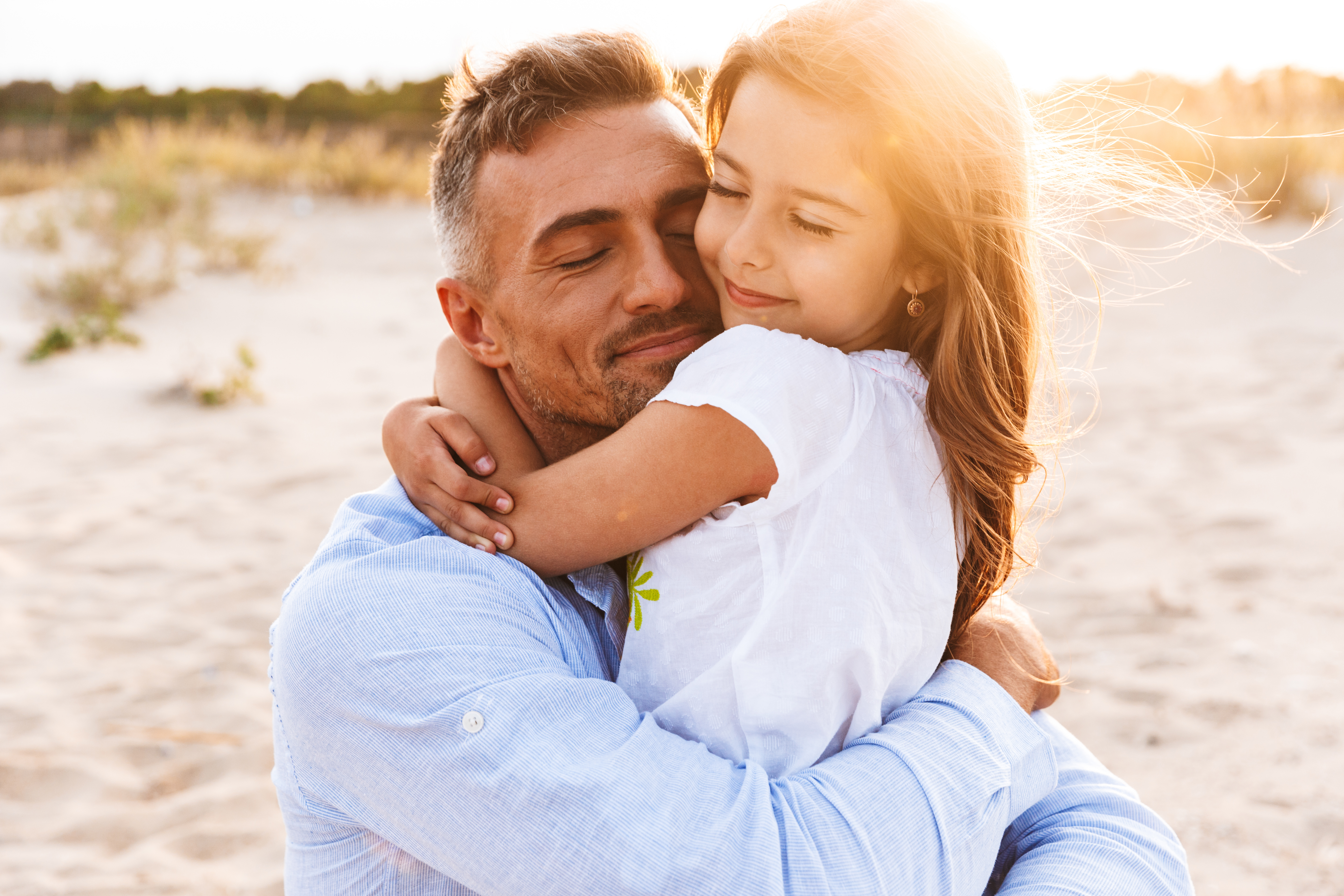 Glücklicher Vater, der seine kleine Tochter am Strand umarmt | Quelle: Shutterstock