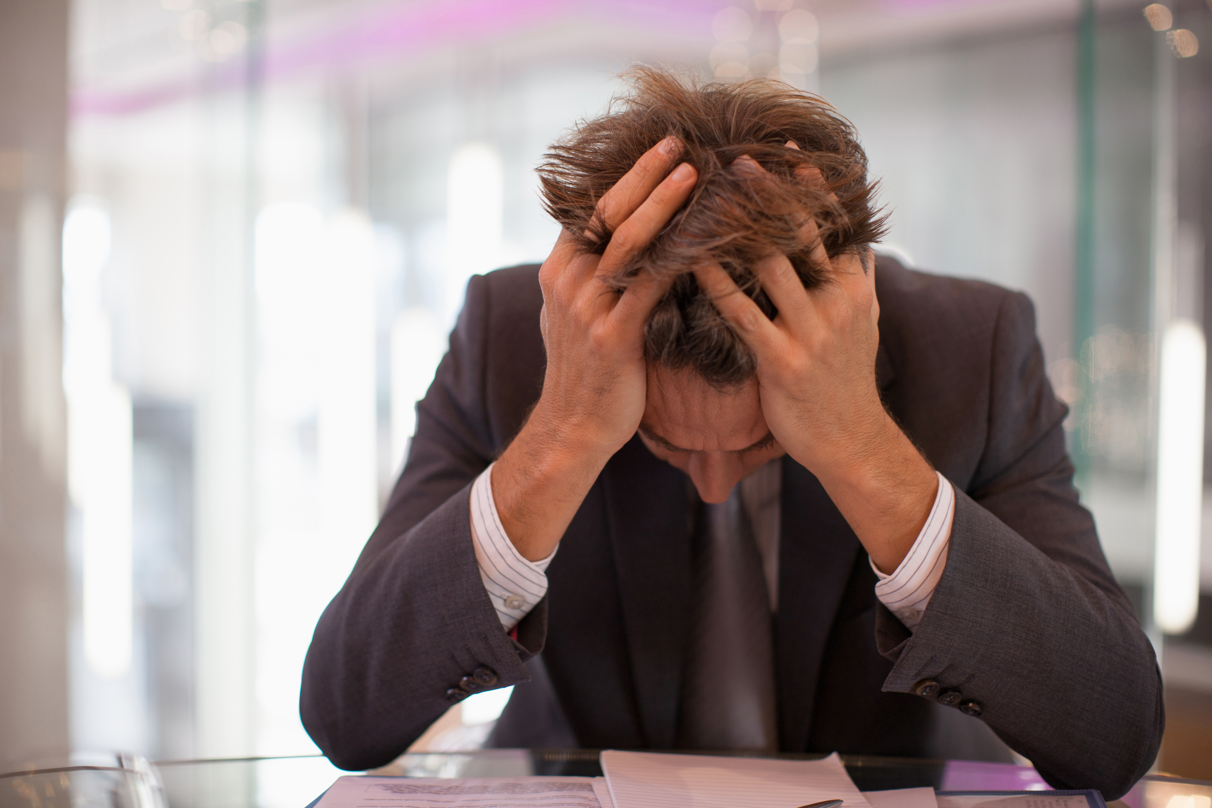 Frustrierter Geschäftsmann, der mit dem Kopf in den Händen am Schreibtisch sitzt | Quelle: Getty Images