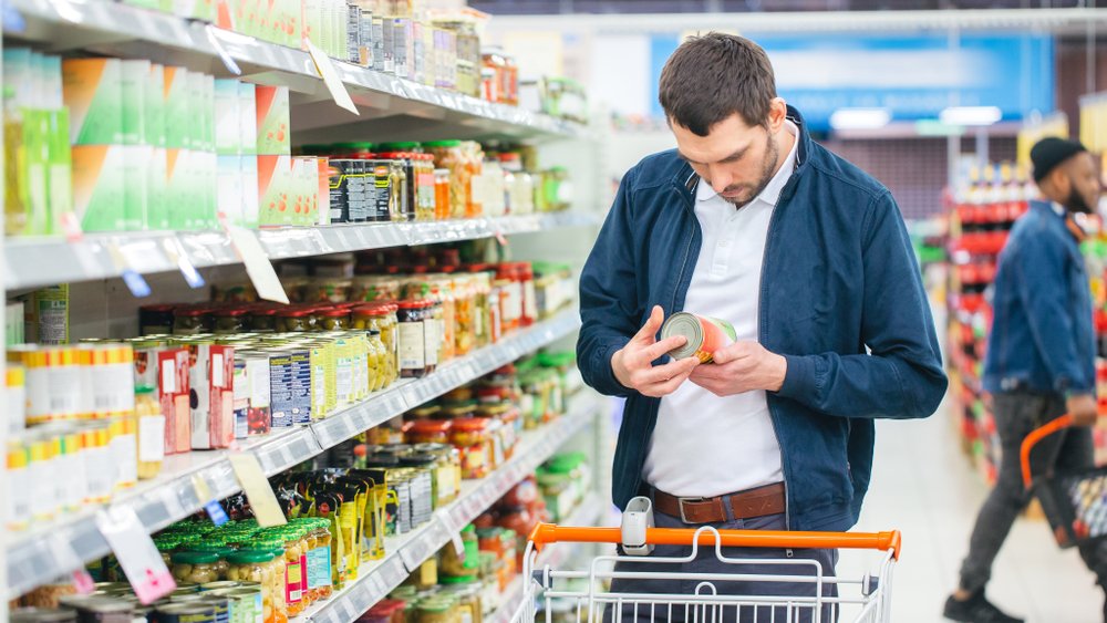 Ein Mann schaut sich eine Dose im Supermarkt an. | Quelle: Shutterstock