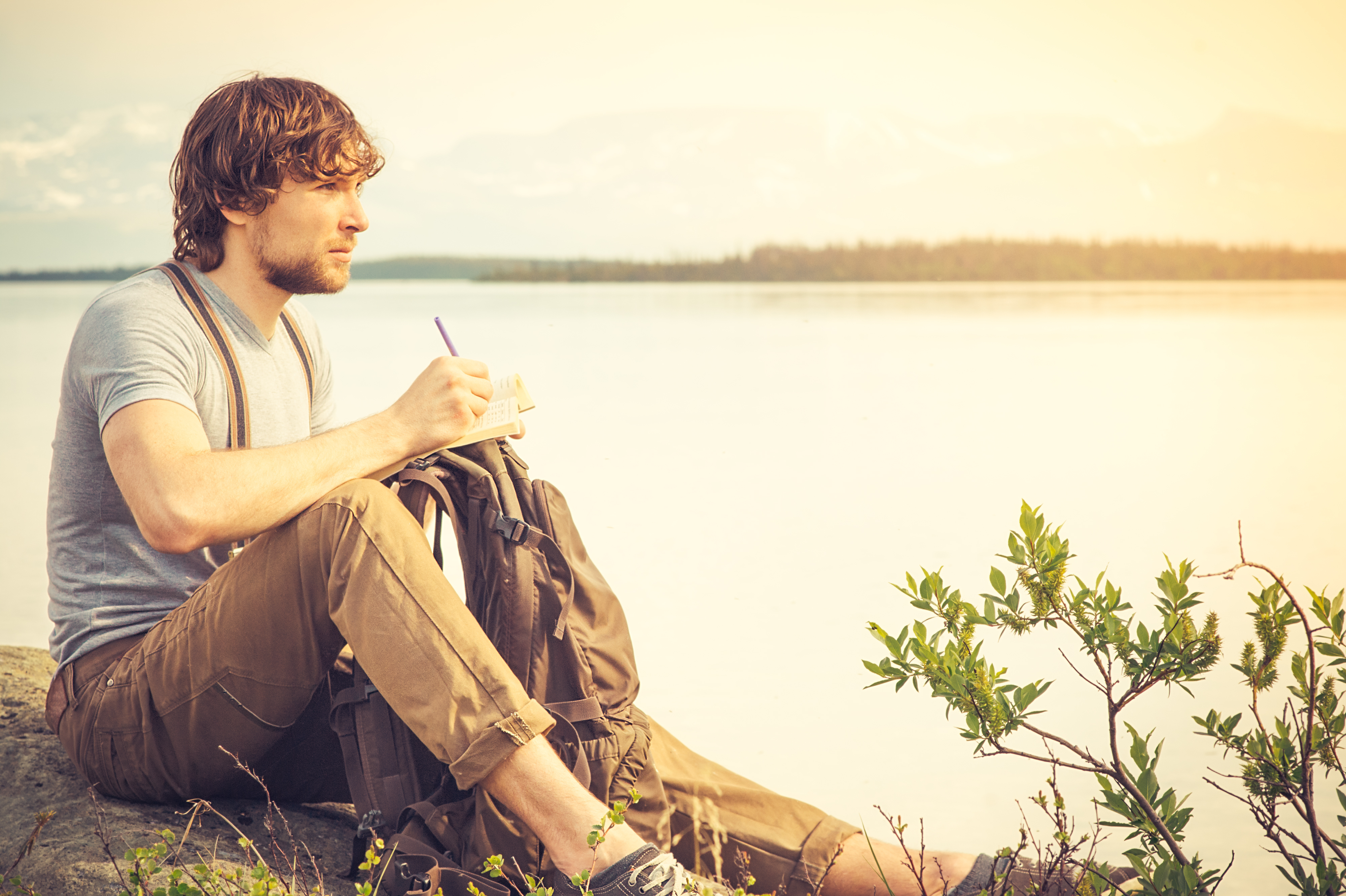 Junger Mann liest ein Buch im Freien mit einem See im Hintergrund | Quelle: Getty Images