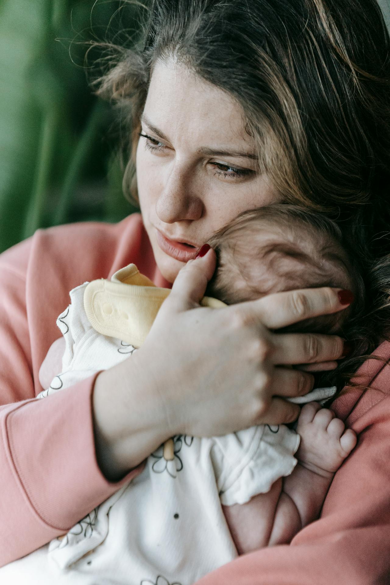Eine traurige, in Gedanken versunkene Frau, die ihr Baby im Arm hält | Quelle: Pexels
