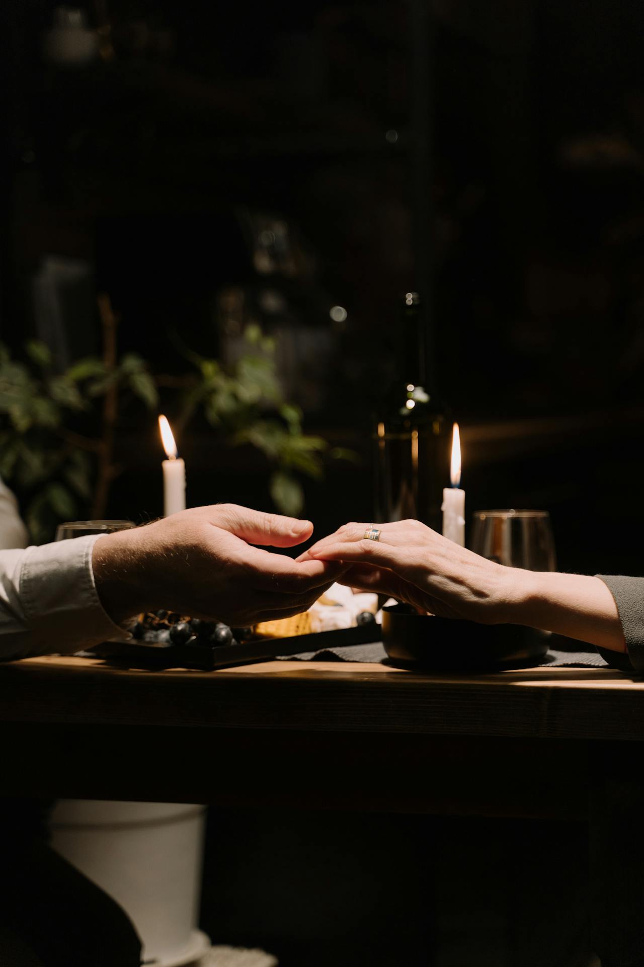 Nahaufnahme eines händchenhaltenden Paares vor der Kulisse eines Abendessens bei Kerzenschein | Quelle: Pexels