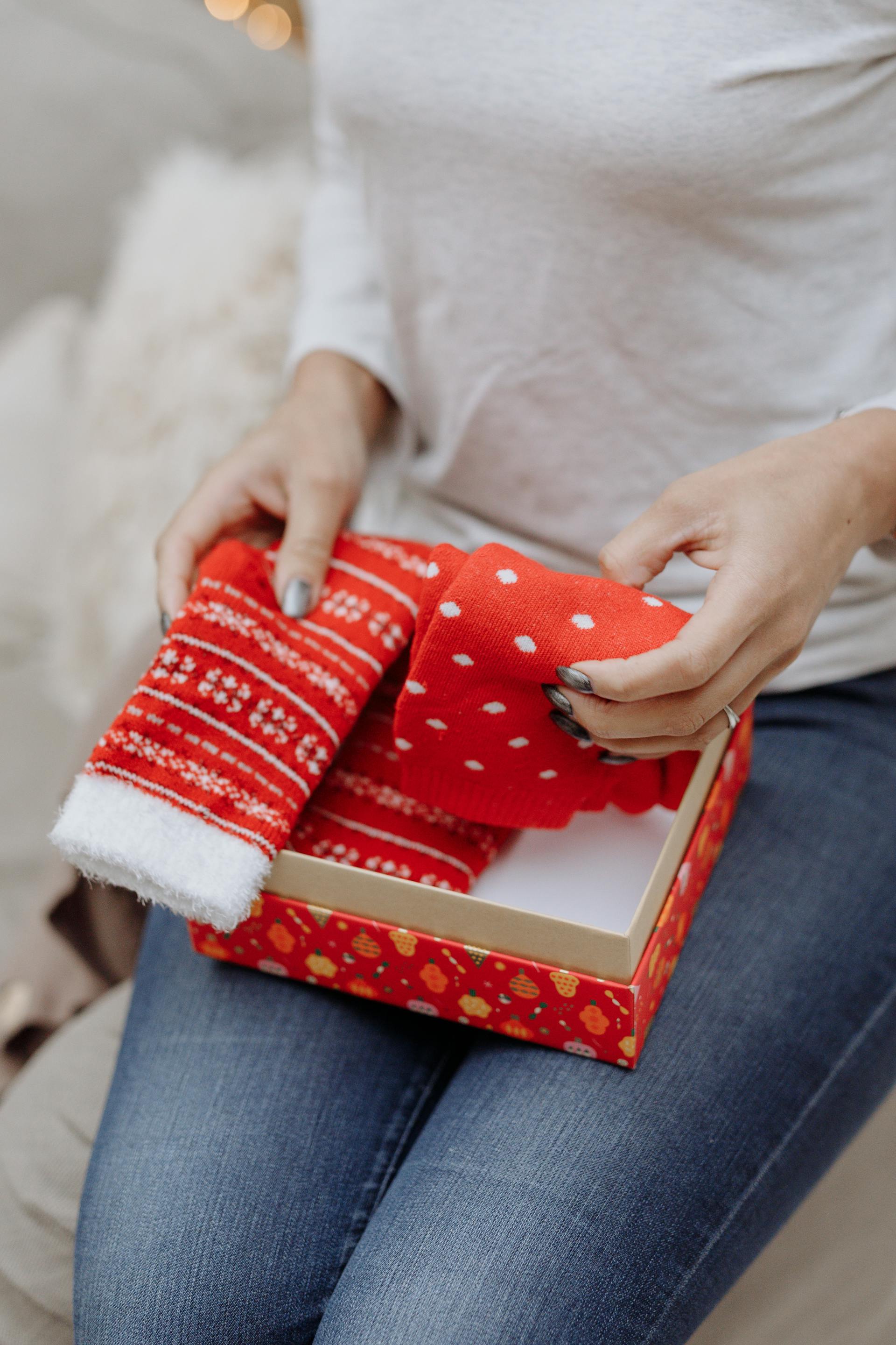 Eine Nahaufnahme einer Frau mit Weihnachtssocken, die in einer roten Geschenkbox liegen | Quelle: Pexels