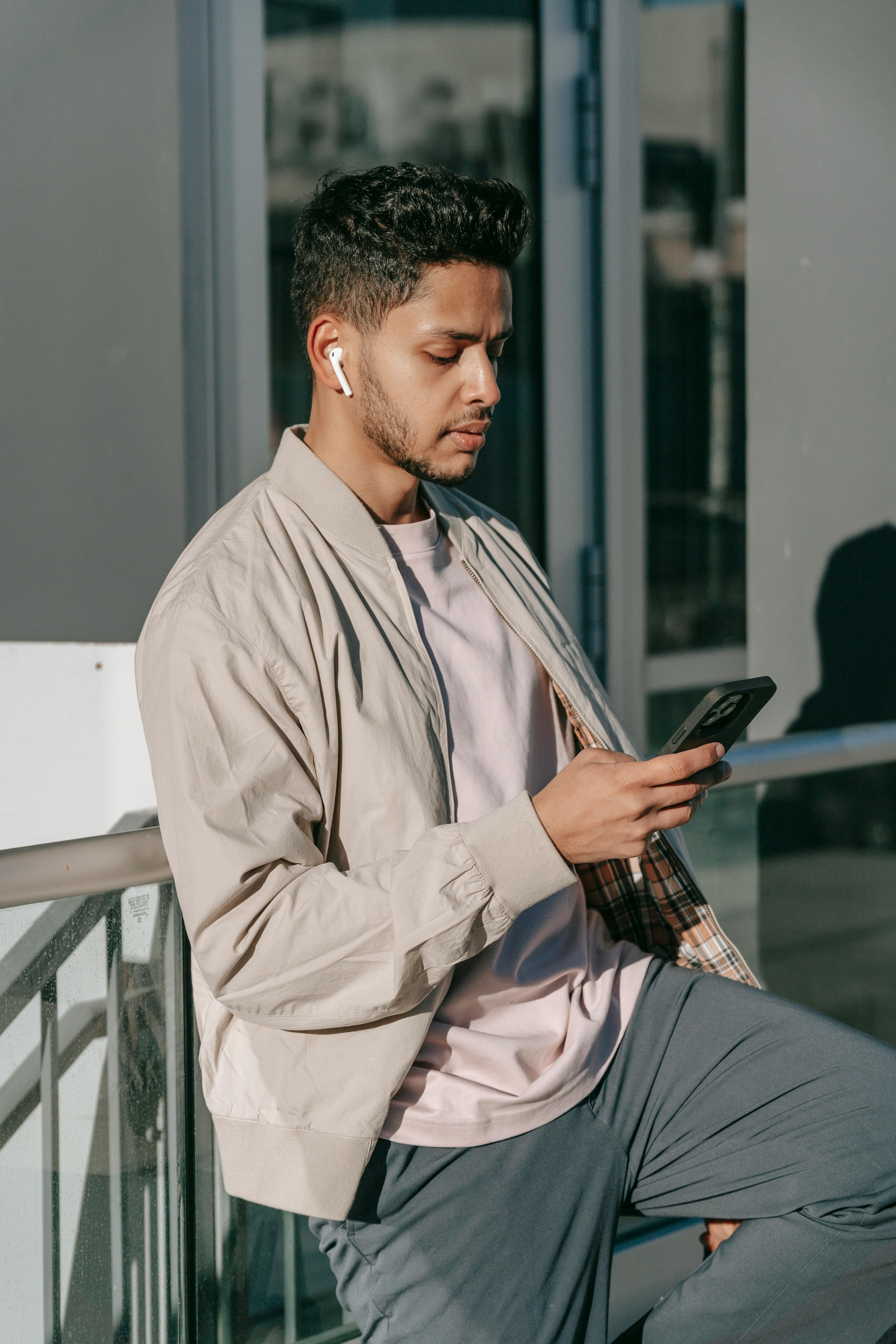 Ein missmutig aussehender Mann, der Ohrstöpsel trägt, während er sein Telefon benutzt | Quelle: Pexels
